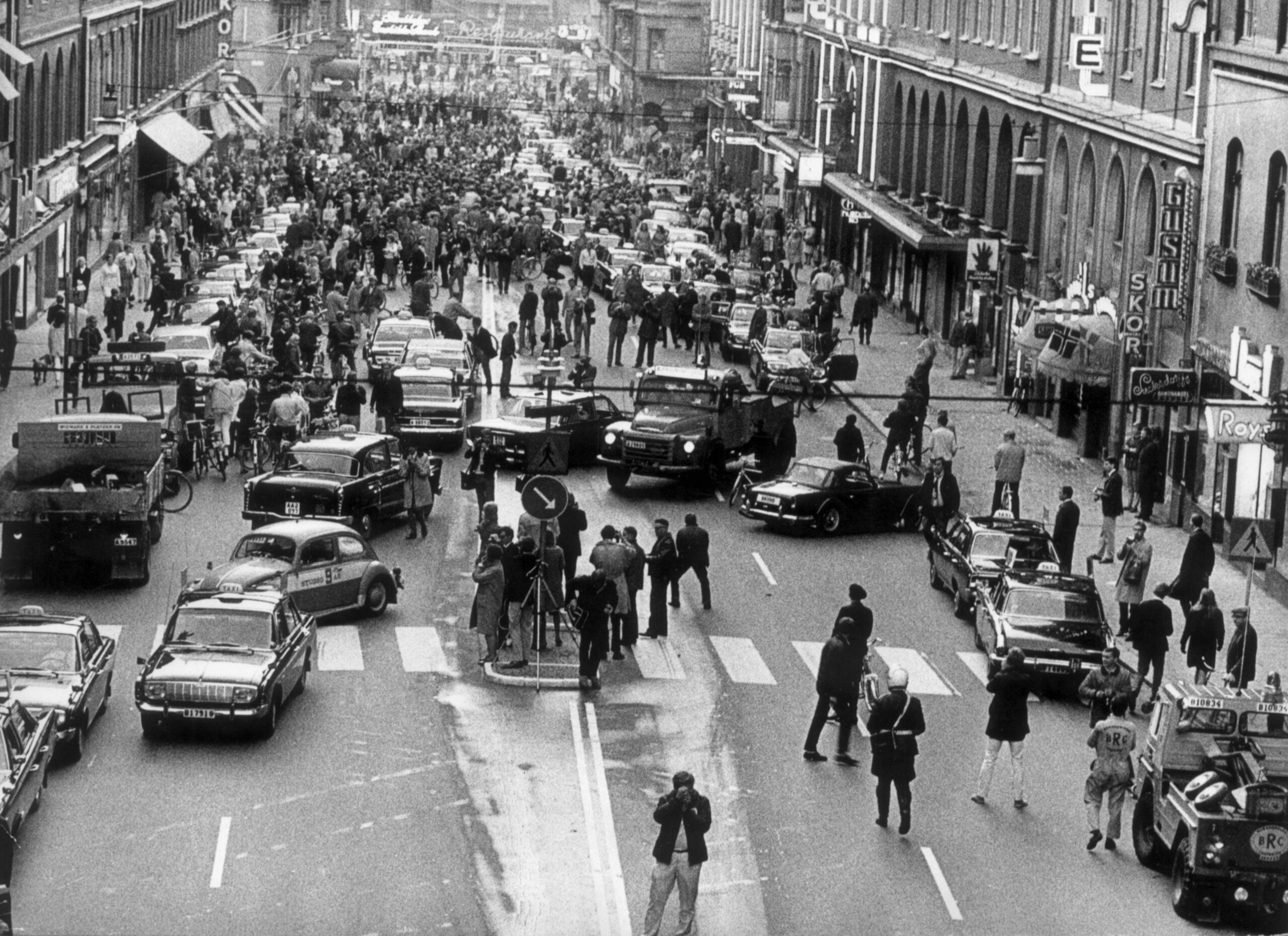 Svartvit bild från Kungsgatan 1967 uppifrån, med tät trafik av bilar och lastbilar som kör på fel sida vid övergången till högertrafik. Stora folkmassor syns längre bort på gatan, samt fotografer och poliser vid en refug i förgrunden.