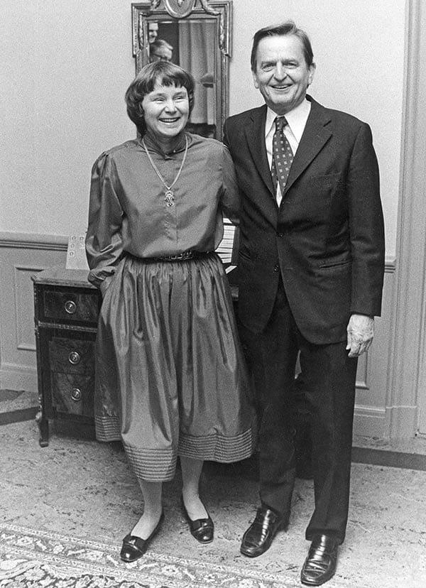 Bild på Olof Palme och hans fru Lisbeth. Bilden är svartvit och de står bredvid varandra. Olof håller armen om Lisbeth
