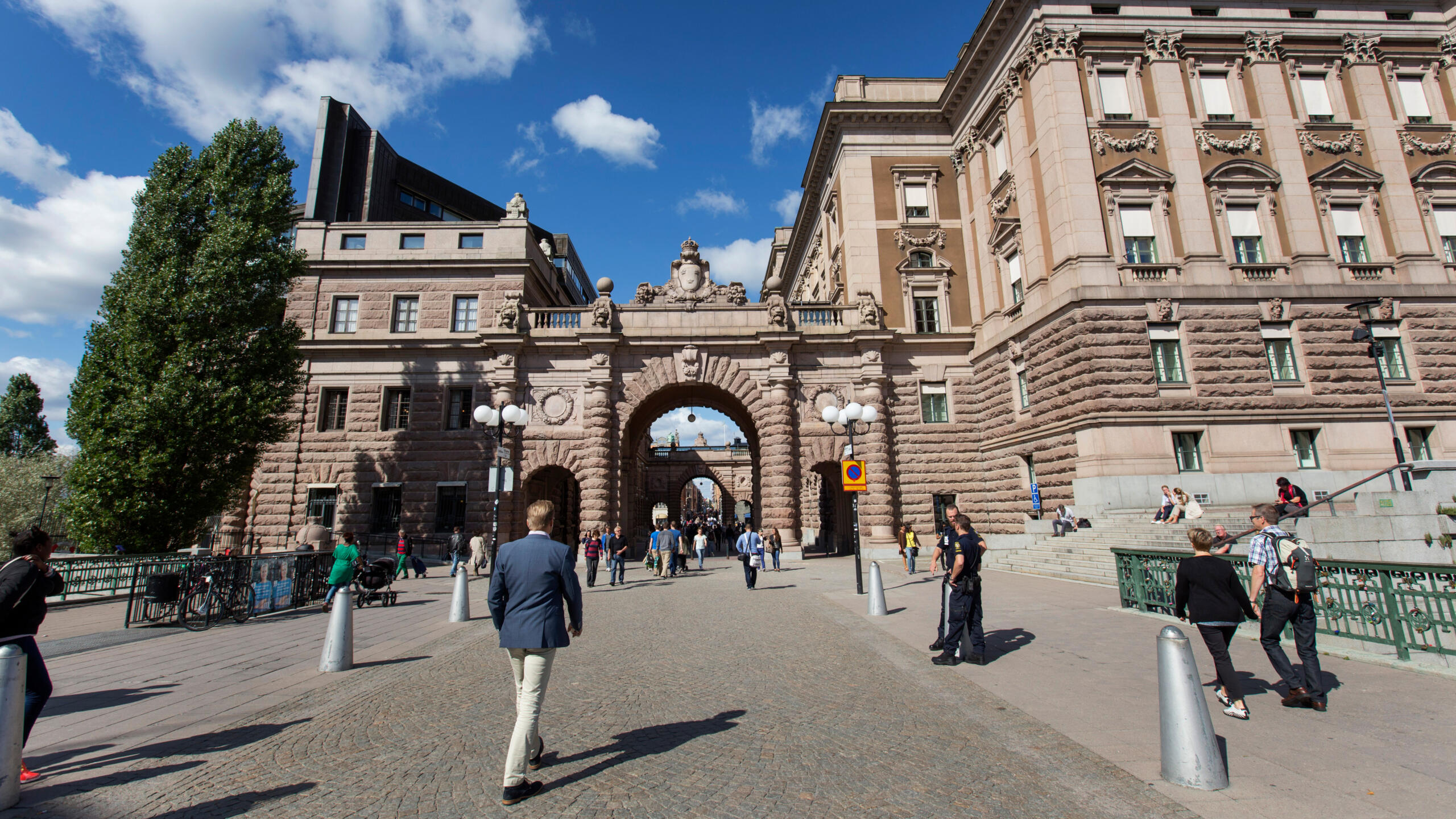 Vy mot Riksdagshuset från Gamla stan. Folk promenerar på Stallbron och Riksgatan.