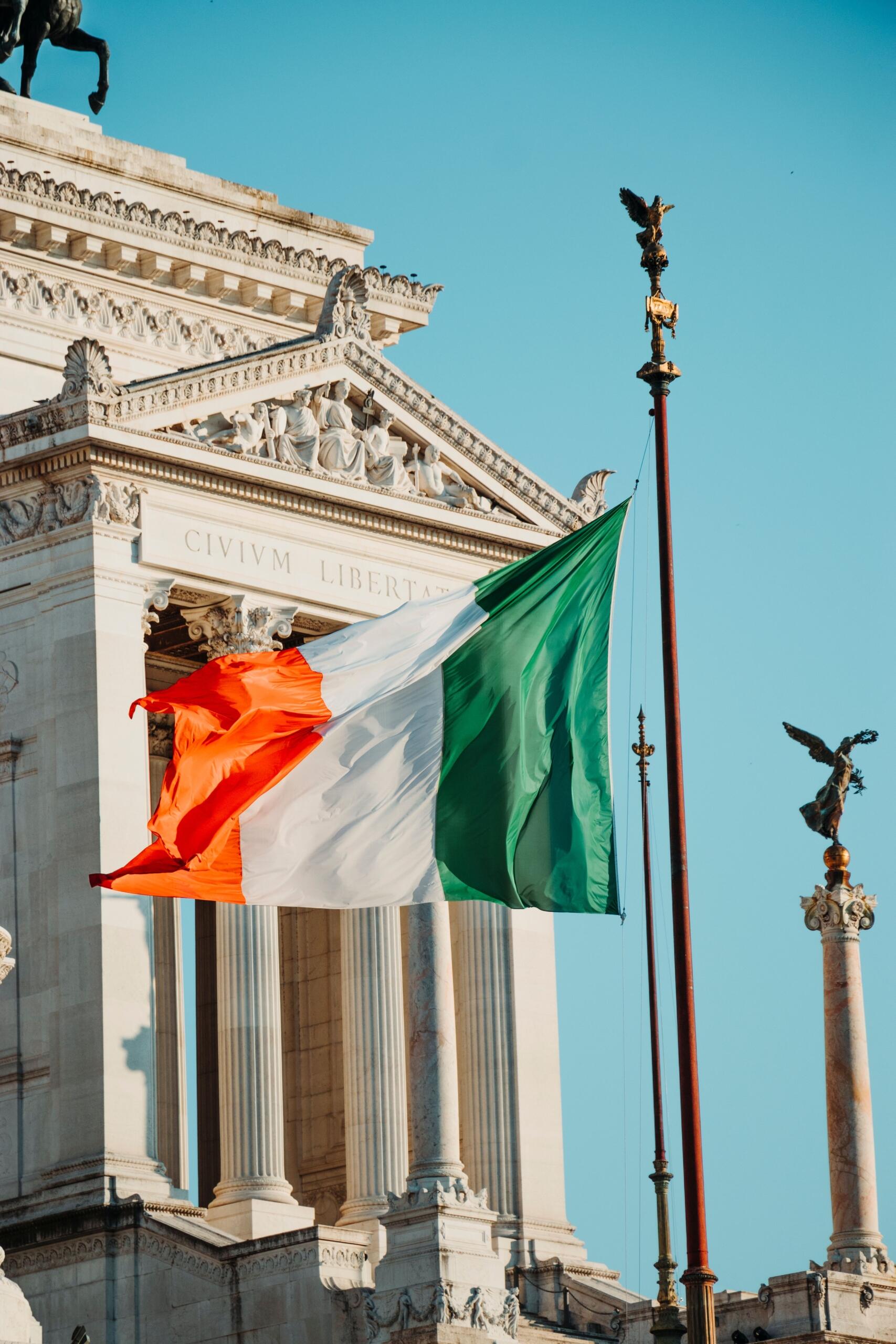 Italiens flagga vajar framför ett monument med vita kolonner i Rom.