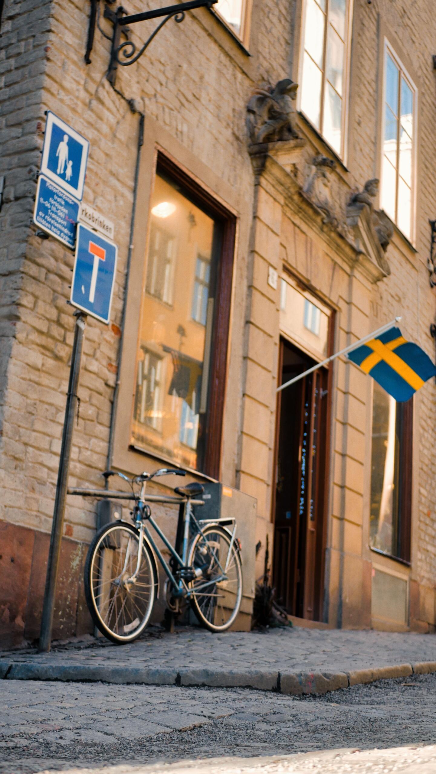 Svensk flagga på en husfasad intill en cykel på en kullerstensgata.