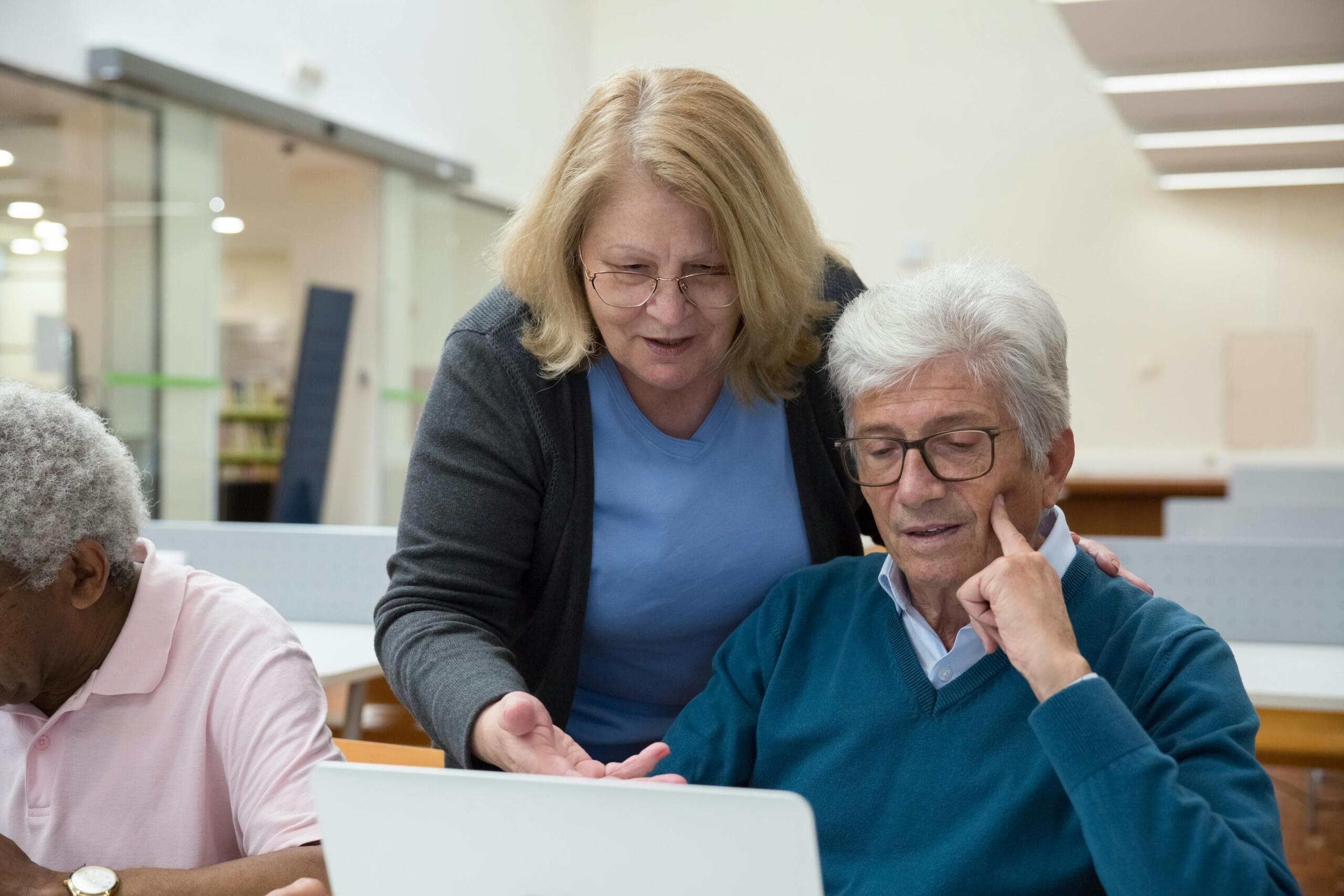 A woman teaching a man how to use a computer.
