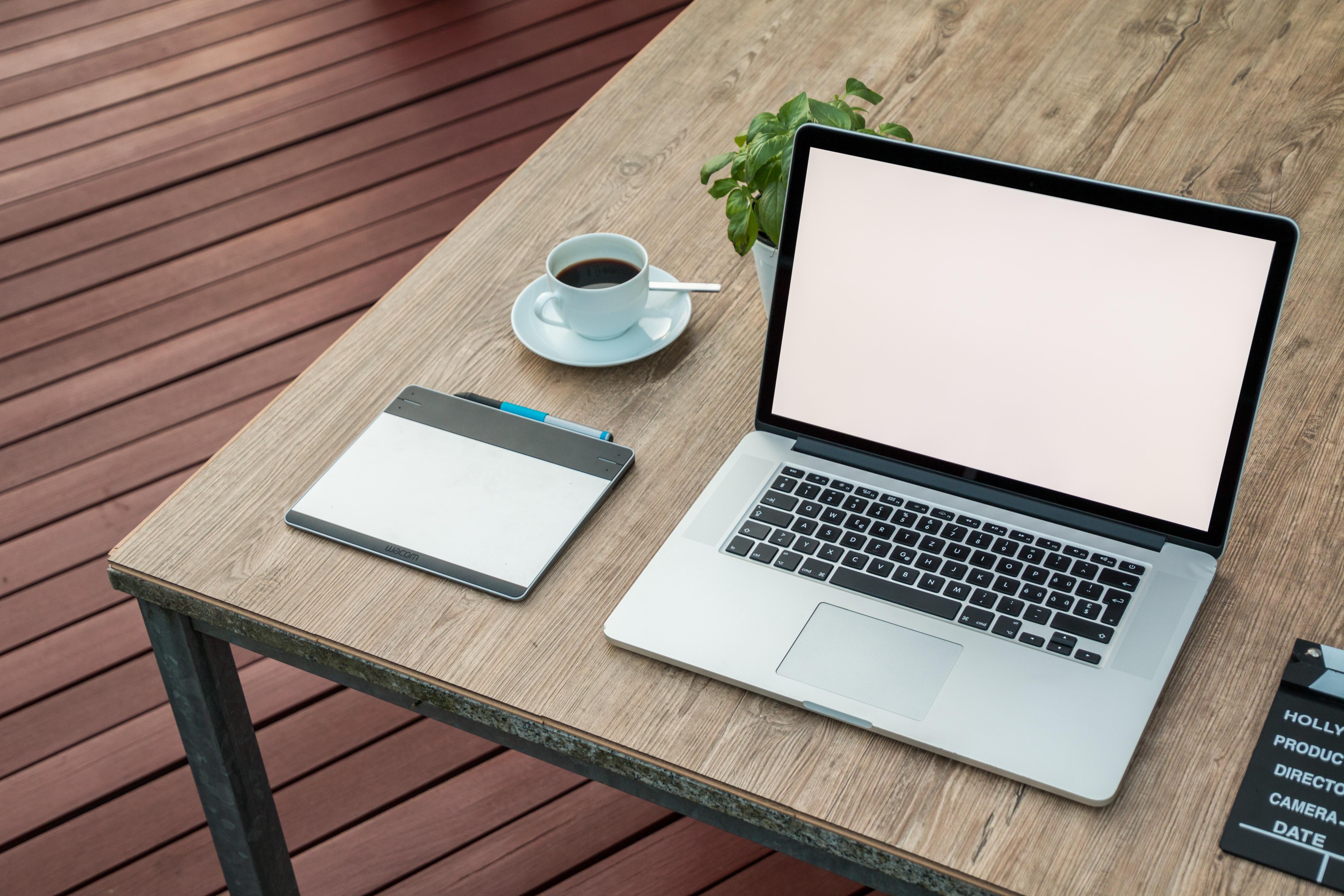 A laptop with a blank white screen, next to a cup of coffee and a notebook on a desk.