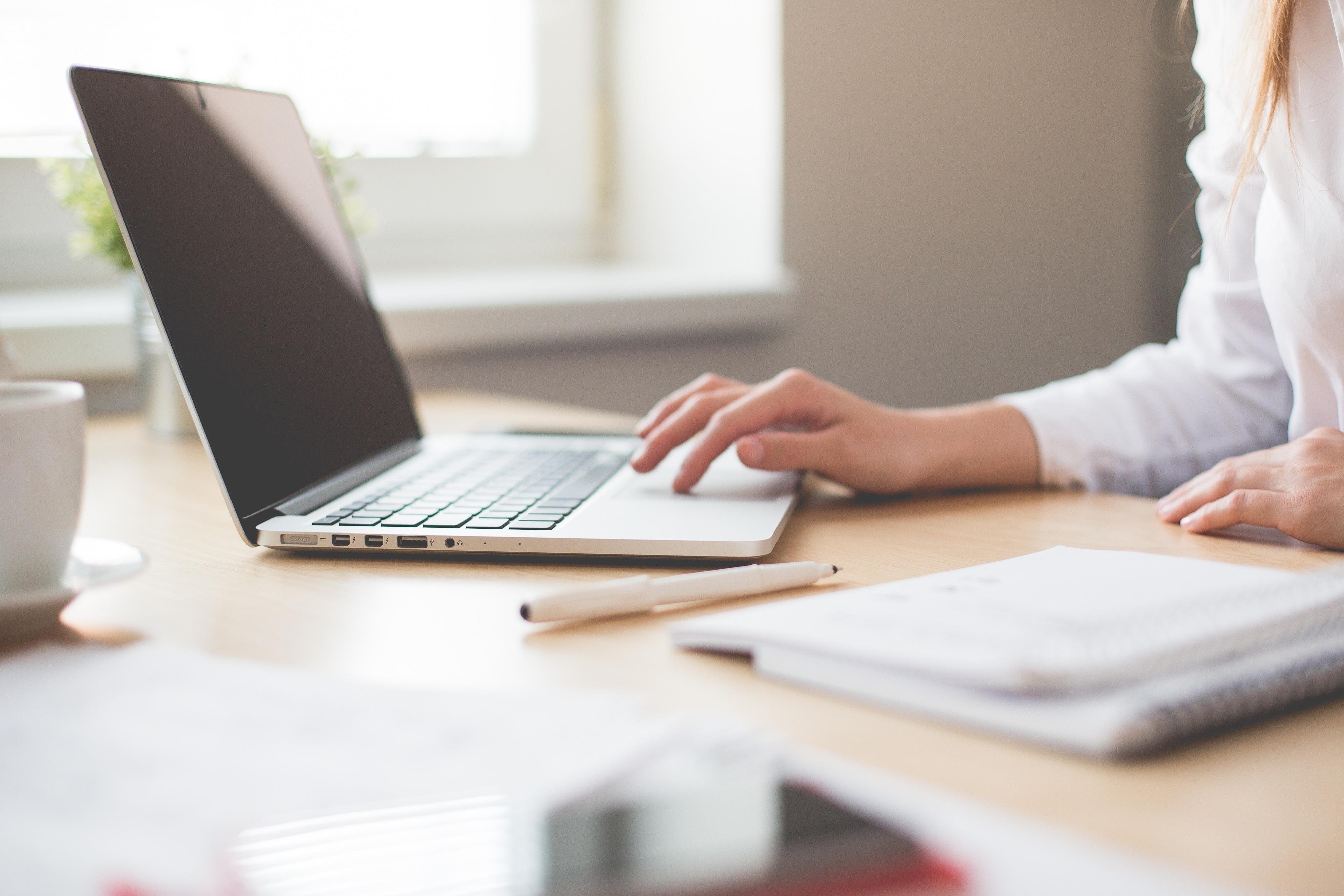 A woman scrolling through a page on her laptop, seated at her desk.
