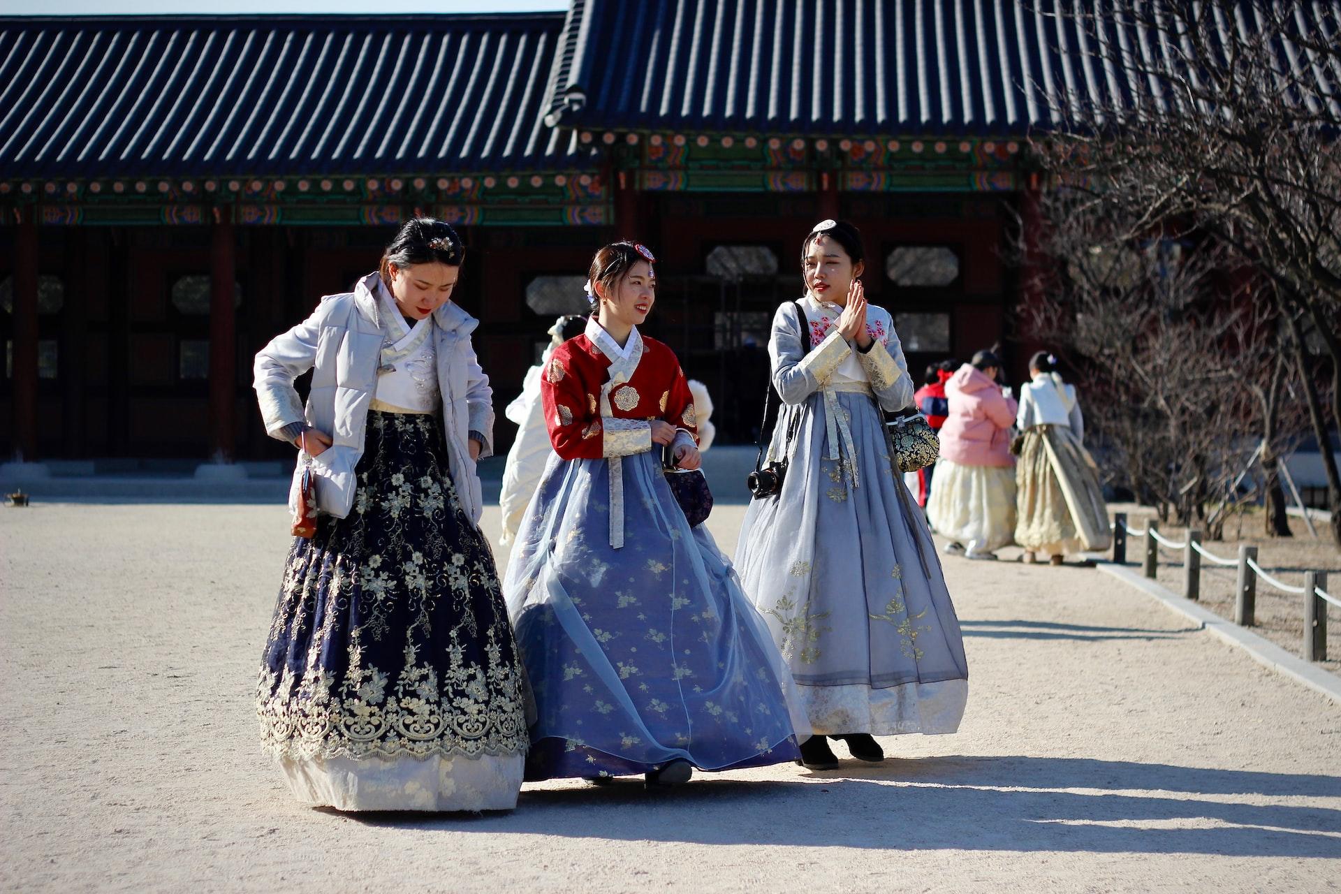 Three women wearing the traditional Korean hanbok on a sunny day at a cultural discovery site. 