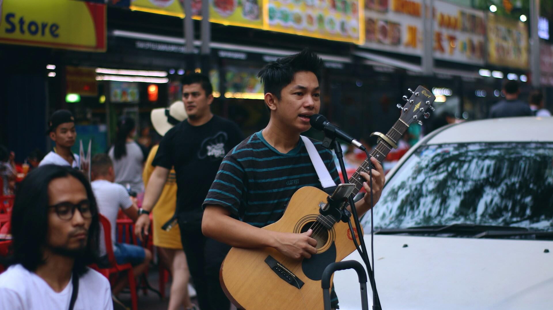 man in black and blue striped shirt playing brown acoustic guitar.