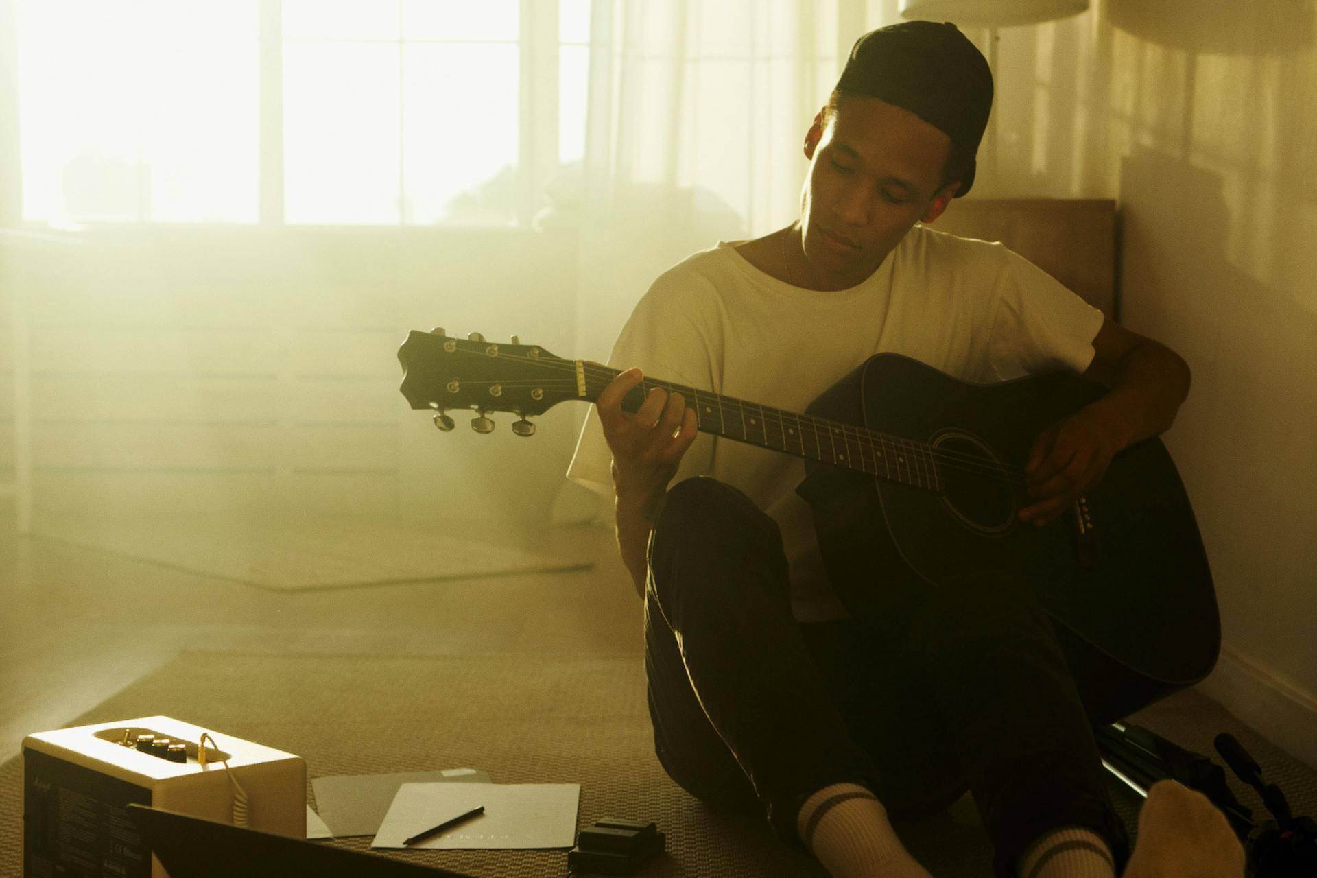 Man in a white T-shirt practicing scales on a black acoustic string instrument.
