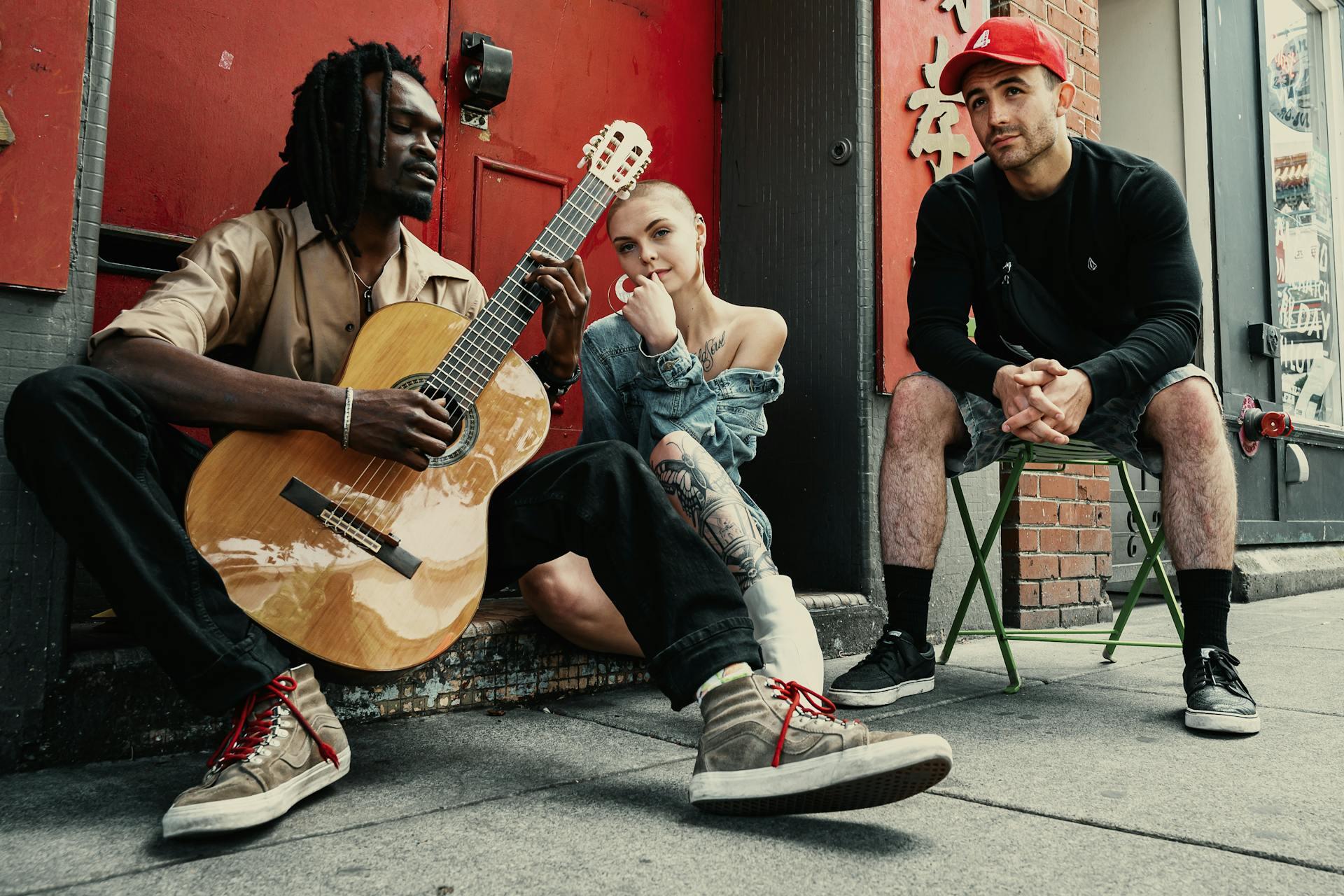 Two Men and Woman Sitting Next to Each Other with one man holding the guitar. 