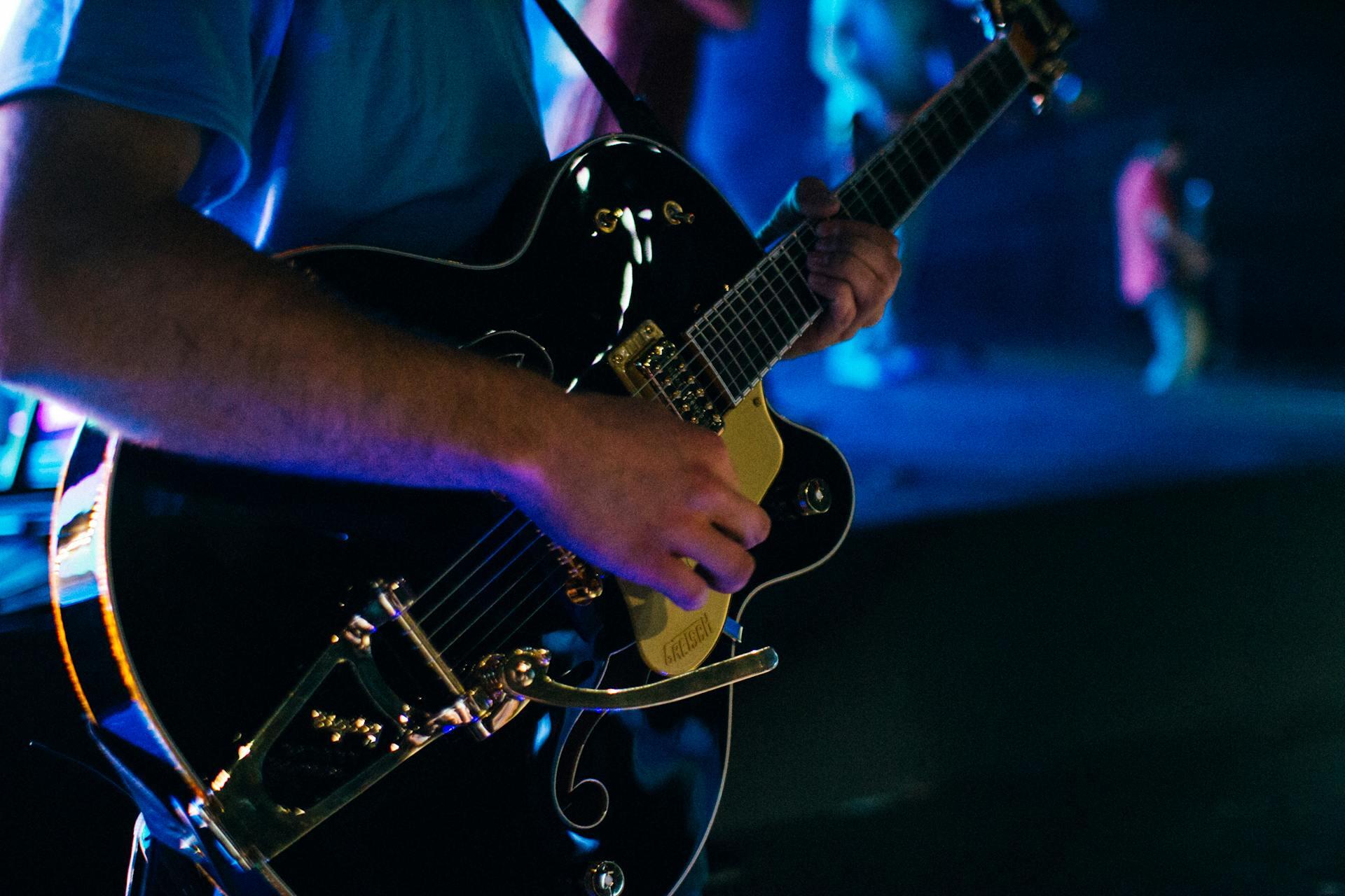Person playing a black electric instrument with visible guitar strings.