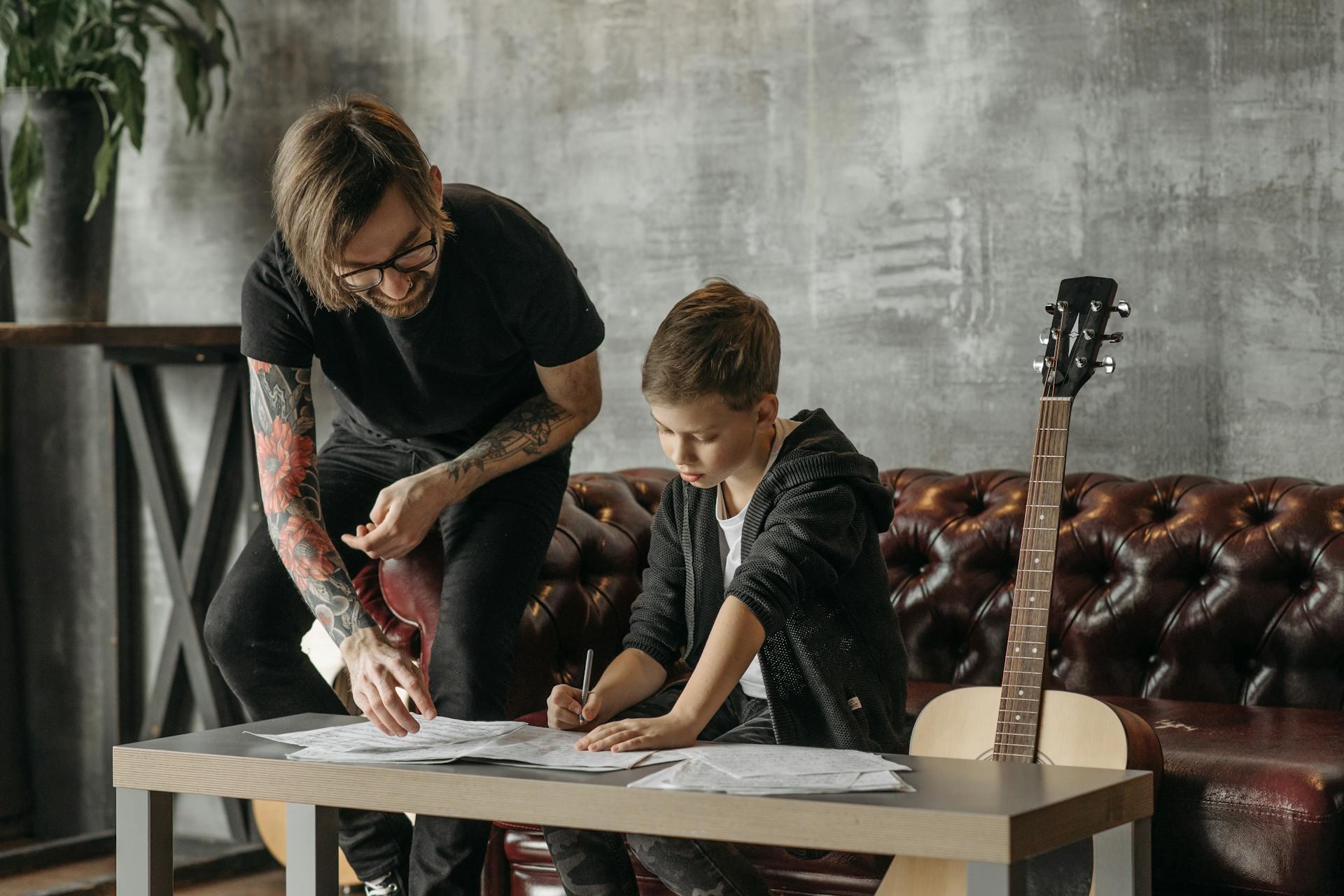 An guitar coach is teaching a boy to play guitar. 