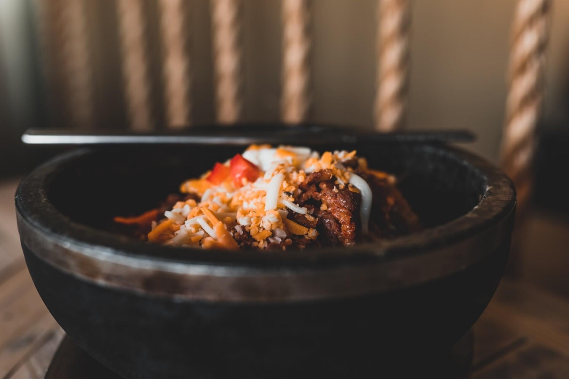 Close-up of Korean bulgogi served in a black stone bowl, garnished with shredded cheese and peppers.