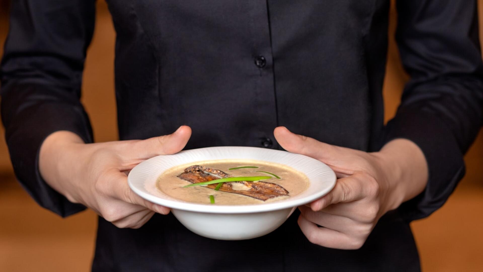 Person holding a bowl of ox bone soup with slices of meat and green onion garnish.