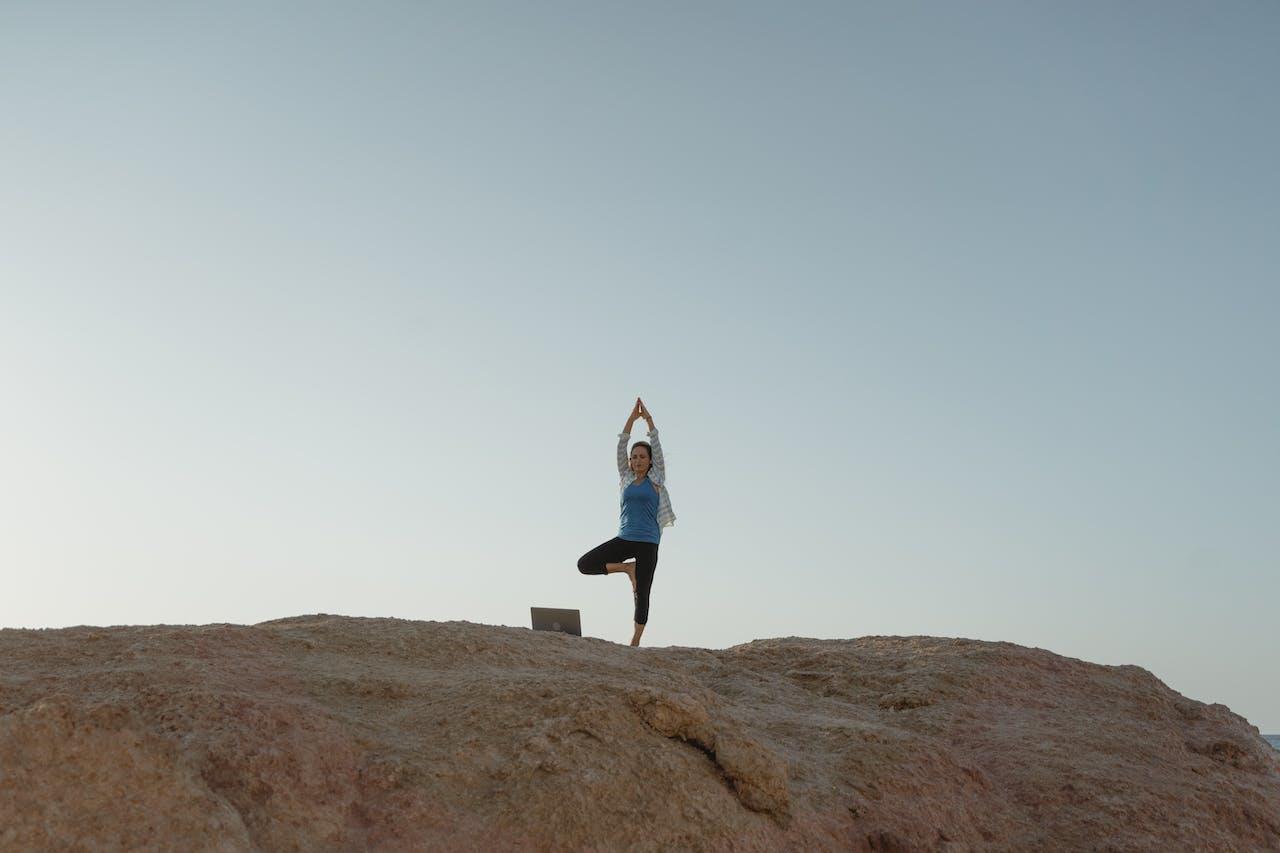 A yogi practising yoga on top of a mountain with their laptop