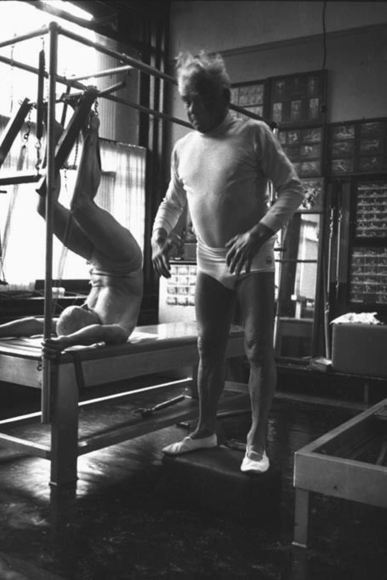 A man performs a handstand in a gym, showcasing strength and balance against a backdrop of gym equipment.