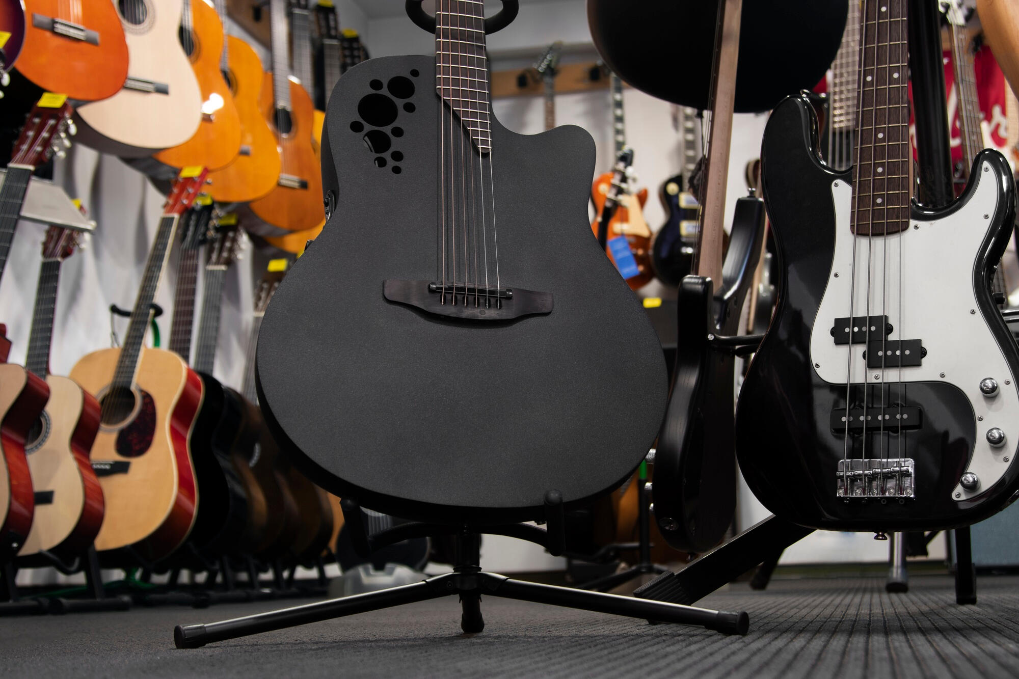 Black acoustic and black-white electric guitars on stands in a music store with various guitars in the background.