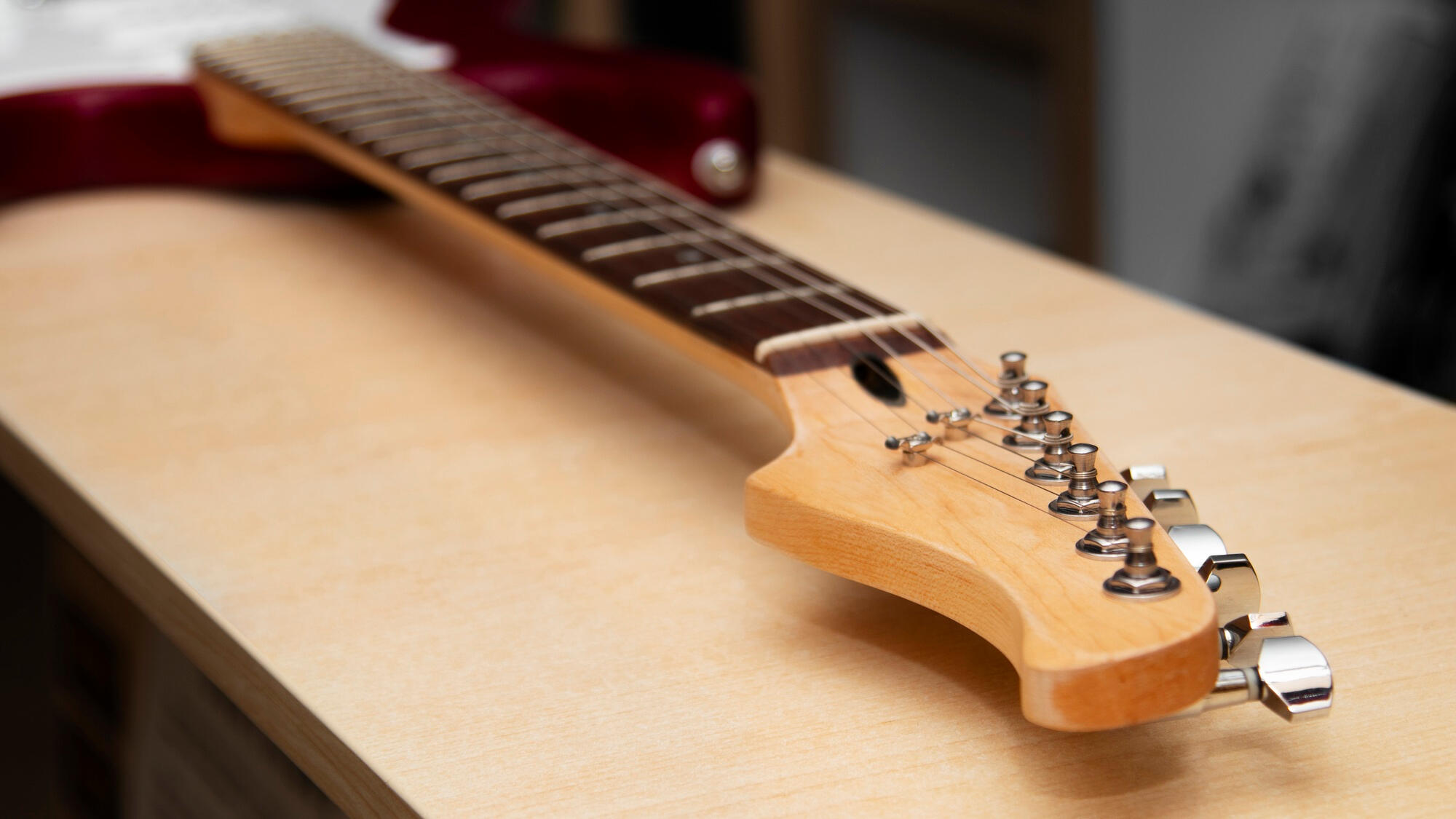 Close-up of an electric guitar's neck and headstock resting on a light wood surface.