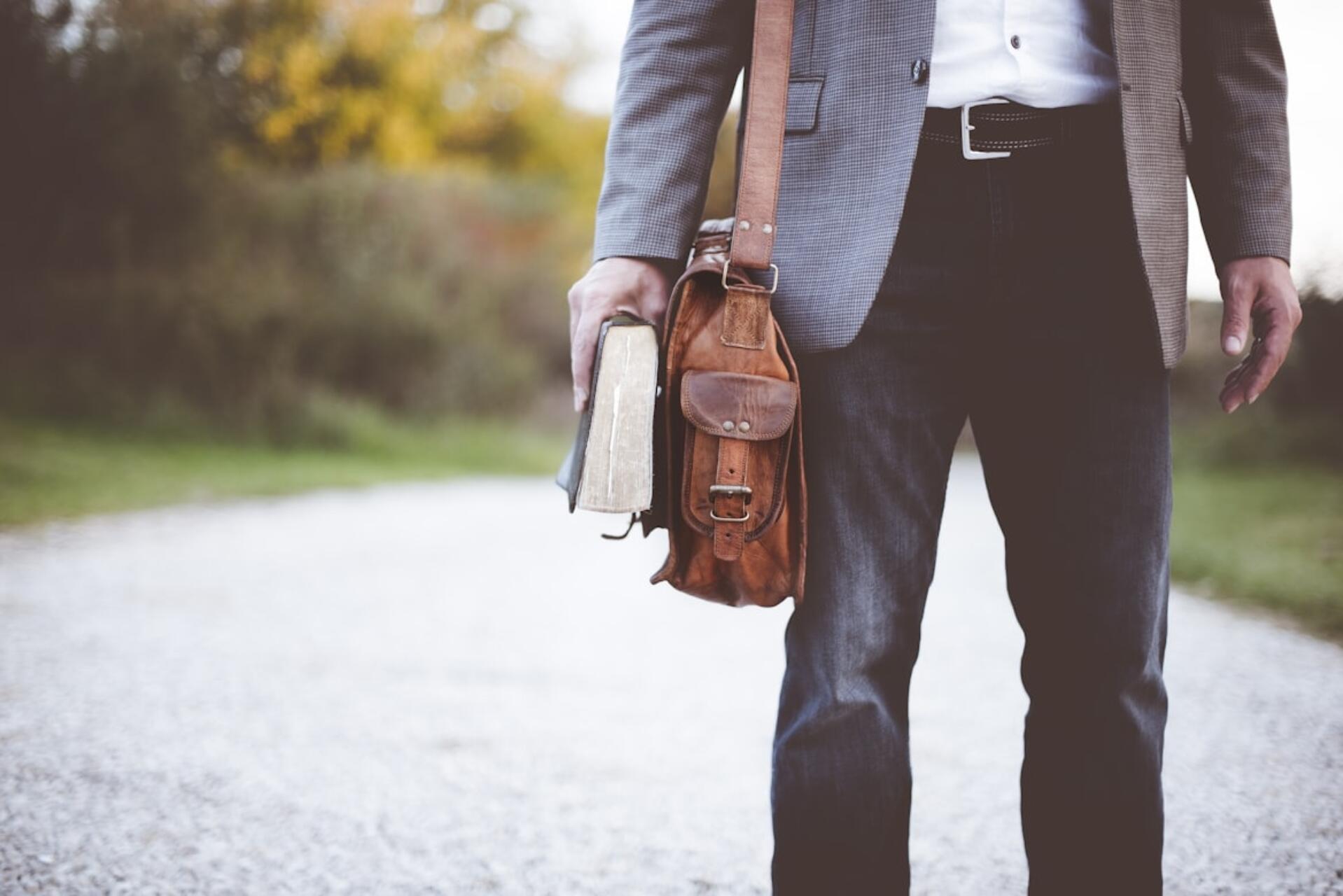 Man in business attire holding a leather briefcase and a book, symbolizing professional career growth in auditing.