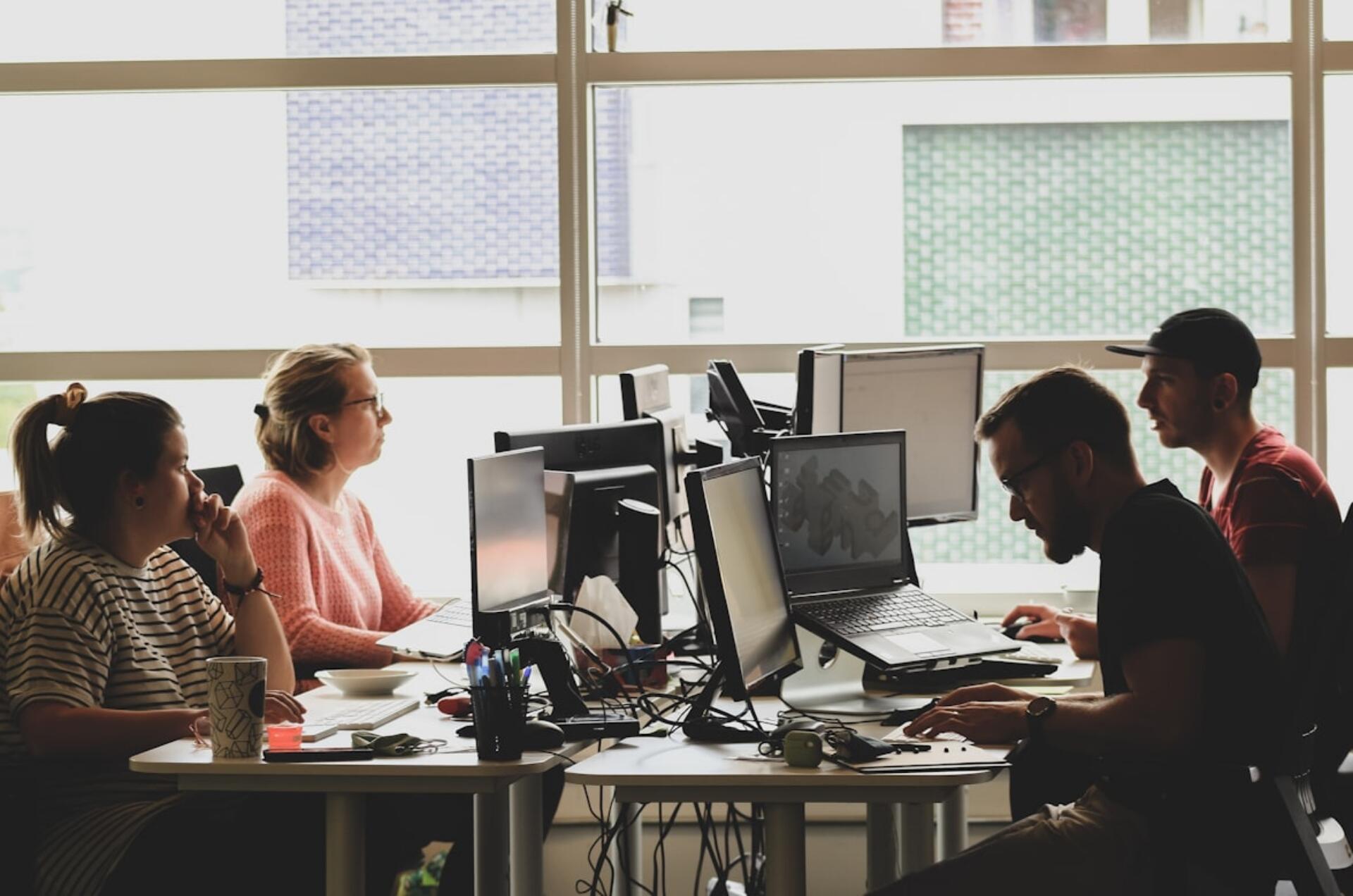 Four people working at desks with computers in a bright modern office