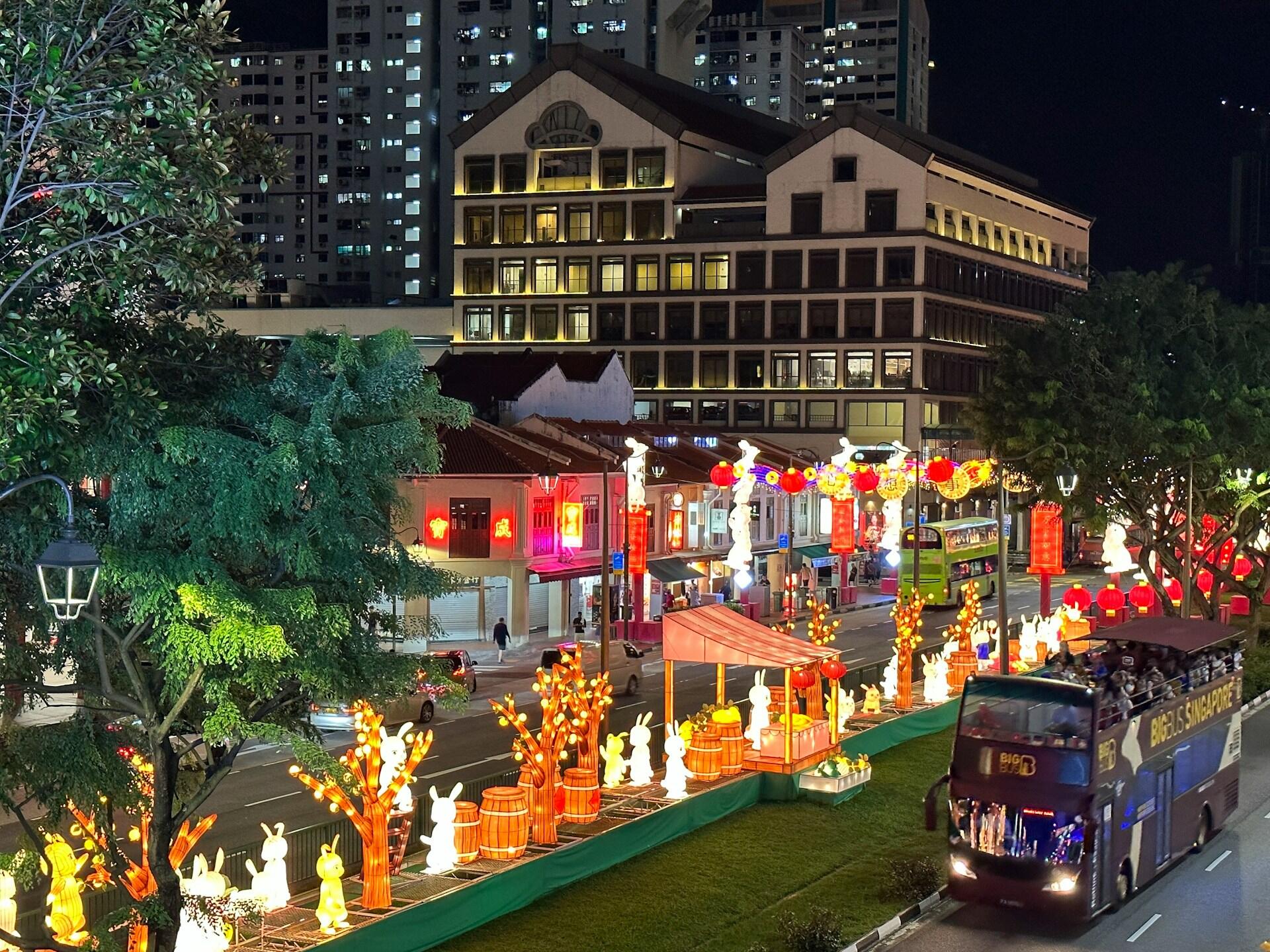 Street at night, brightly decorated with illuminated rabbit statues and lanterns. Festive atmosphere with a bus and city buildings in the background.