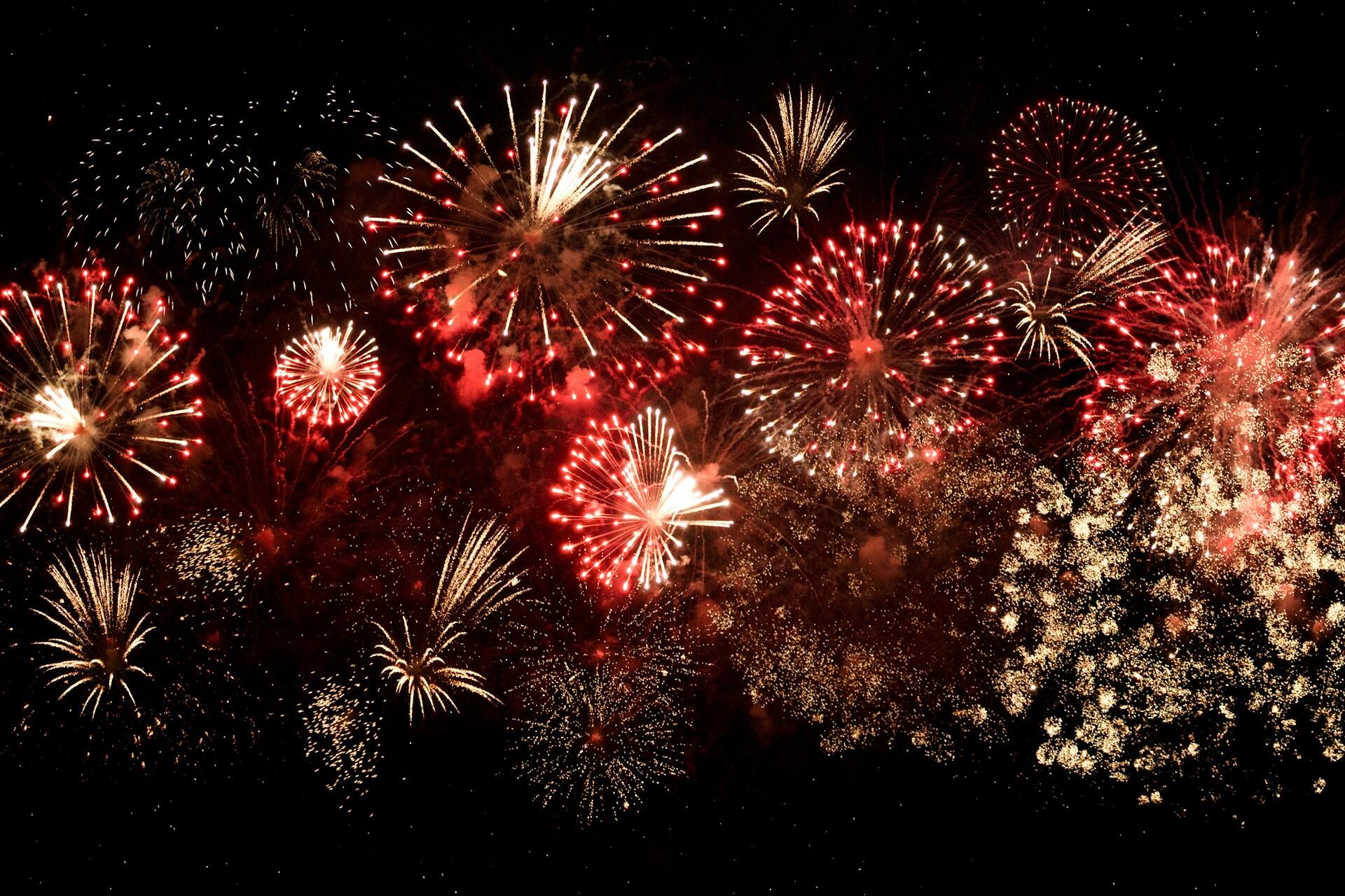 A vibrant display of red and gold fireworks bursts across a dark night sky, creating a dazzling and festive atmosphere of celebration.