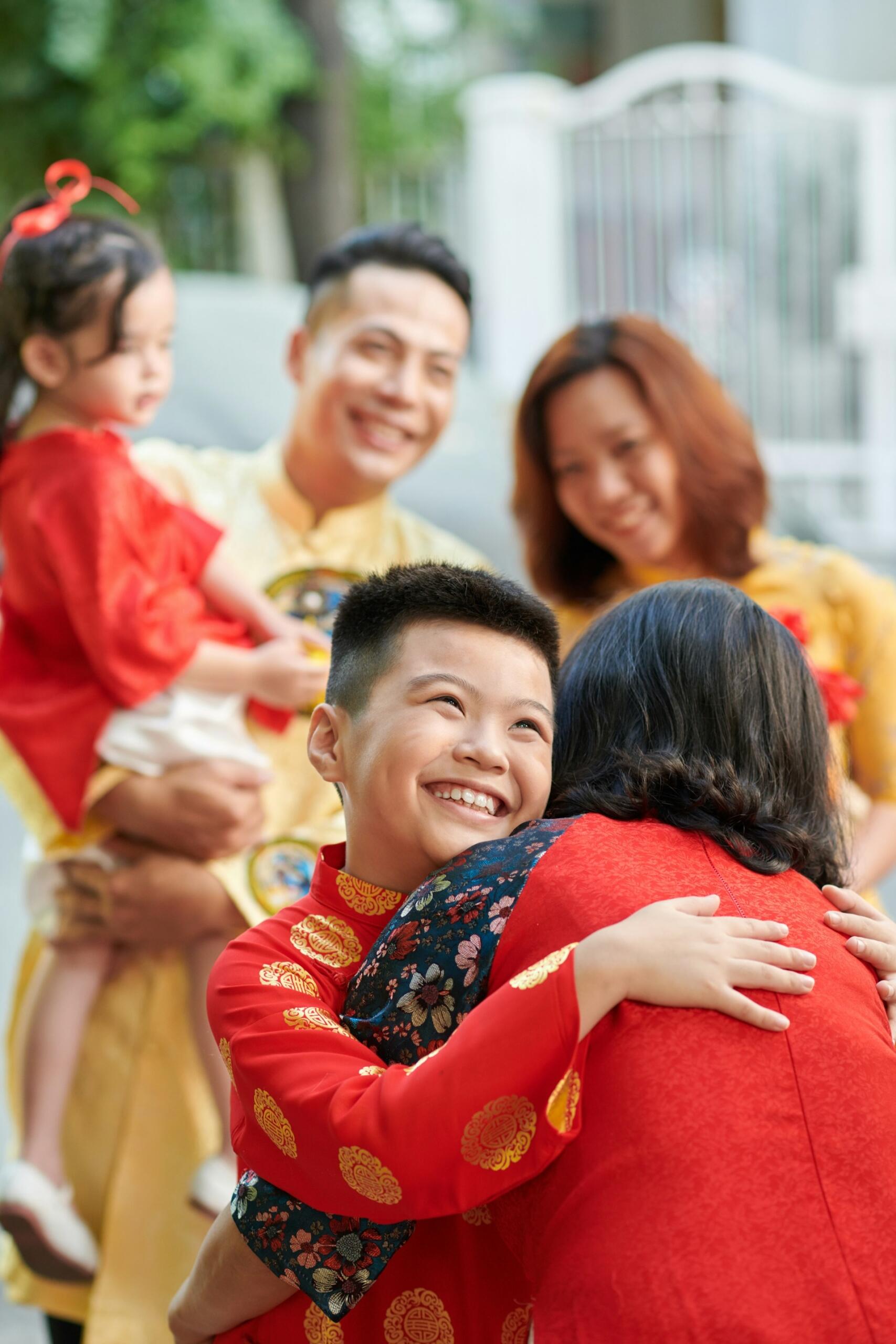A woman wearing red hugs a child while adults wearing gold smile in the background.