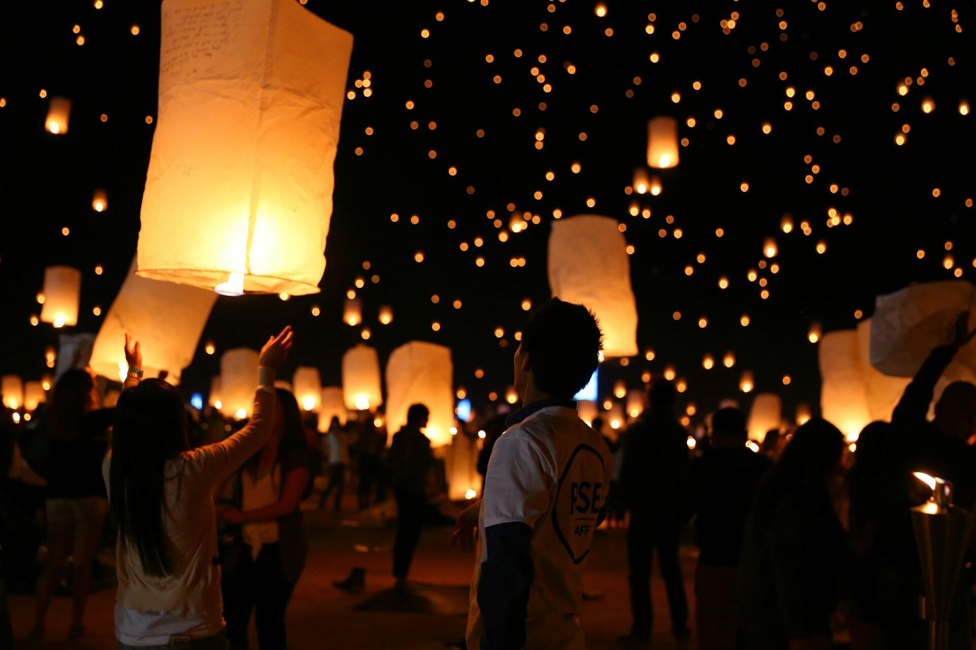 People release glowing lanterns into a starry night sky, creating a warm, festive atmosphere filled with awe and wonder.