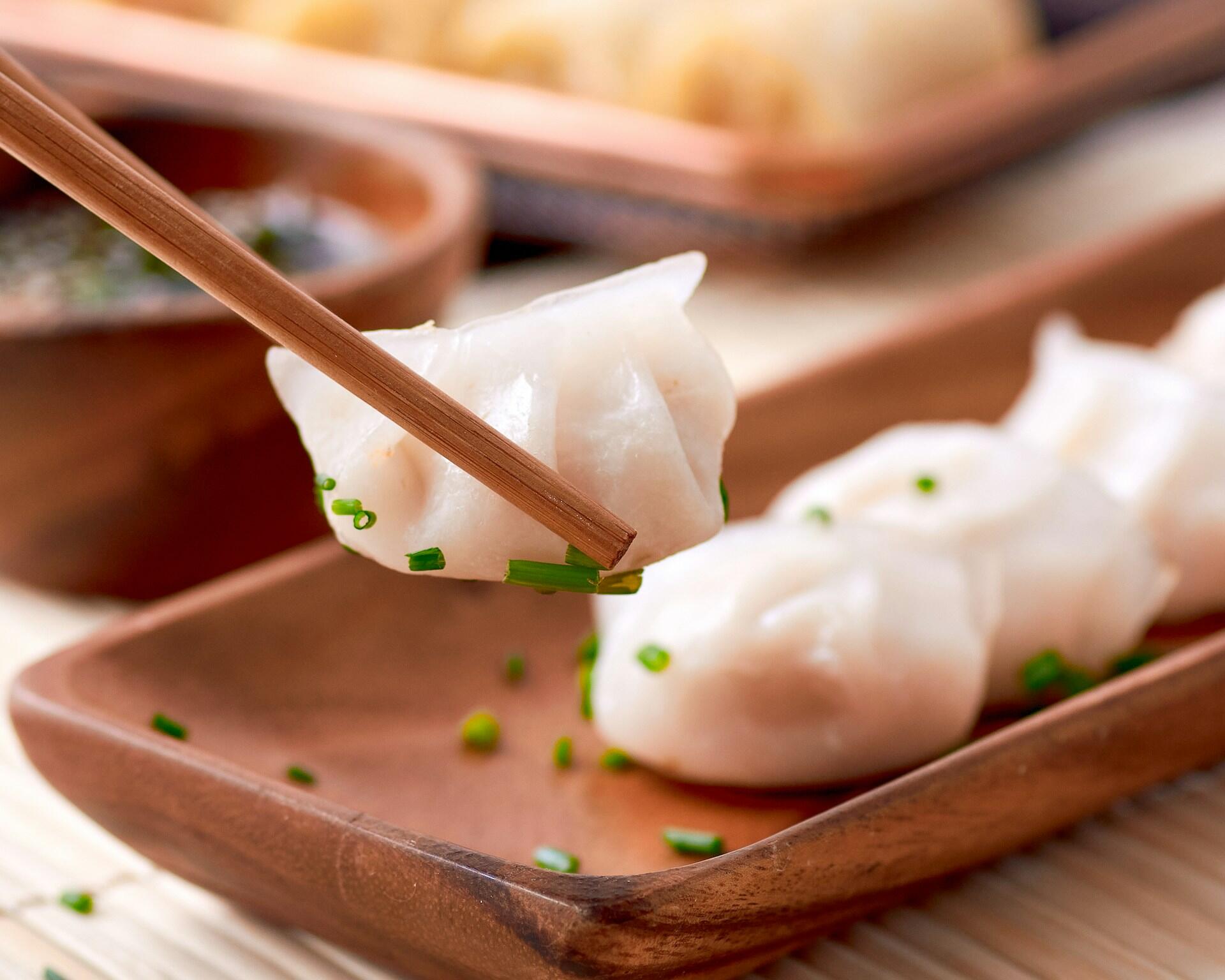 Dumplings on a wooden plate with one between chopsticks.
