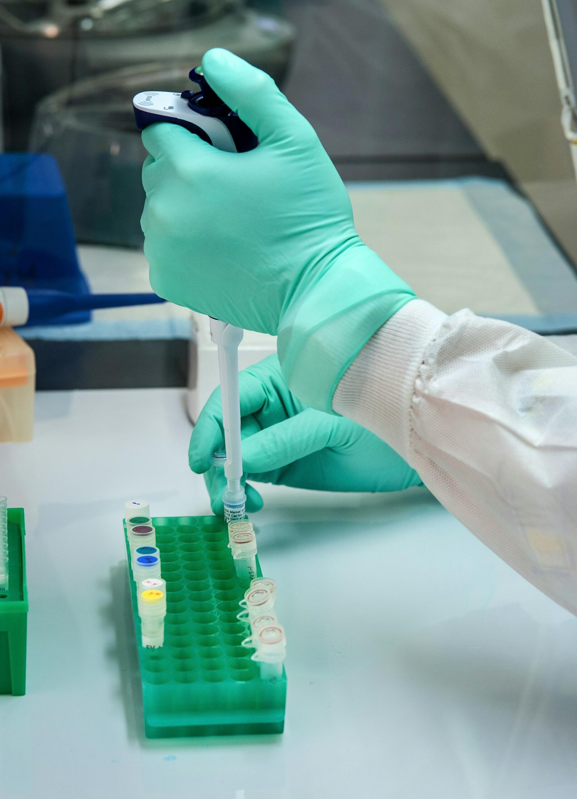 A person with green safety gloves works at a lab bench.
