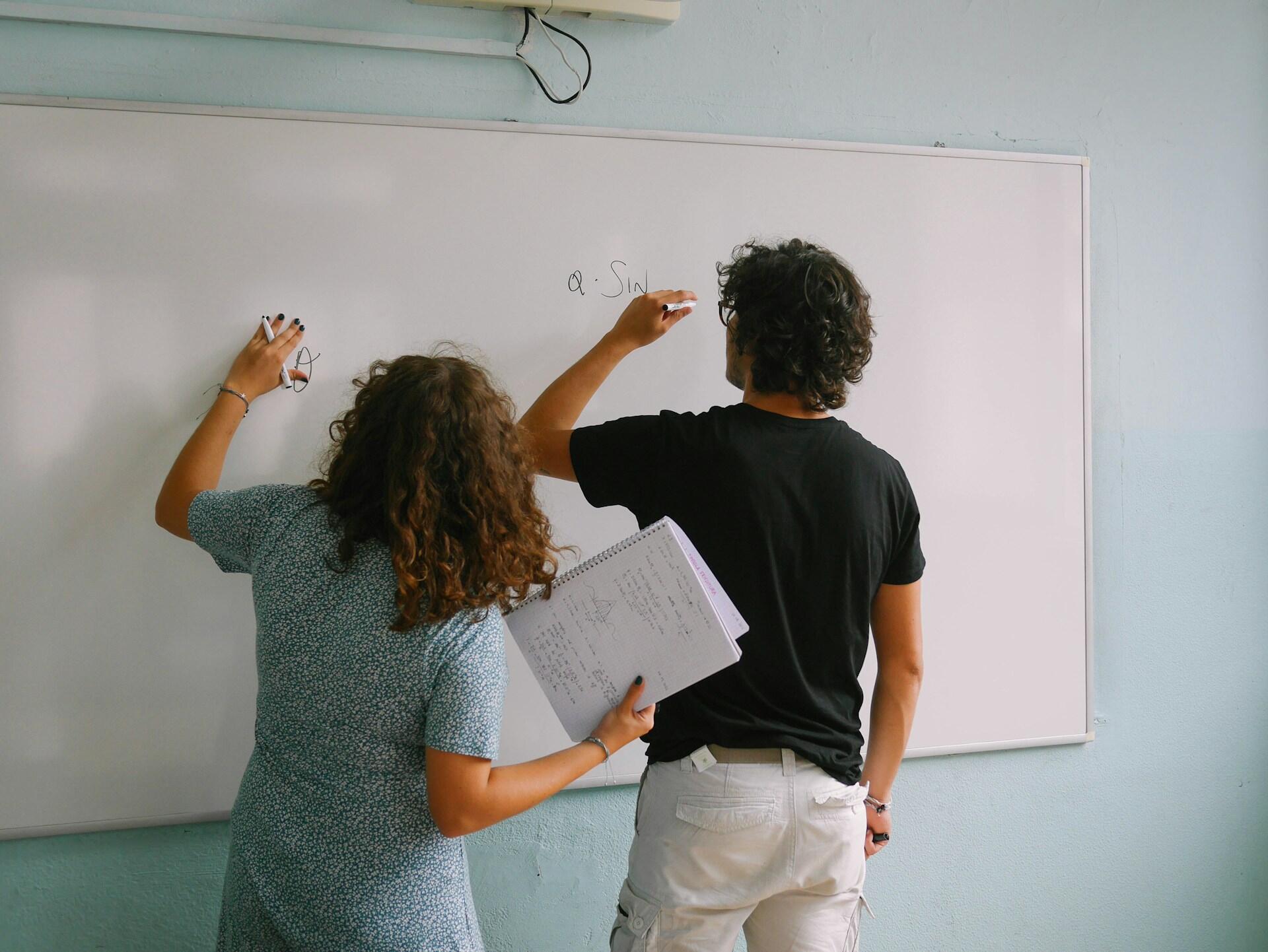 Two people writing on a whiteboard.