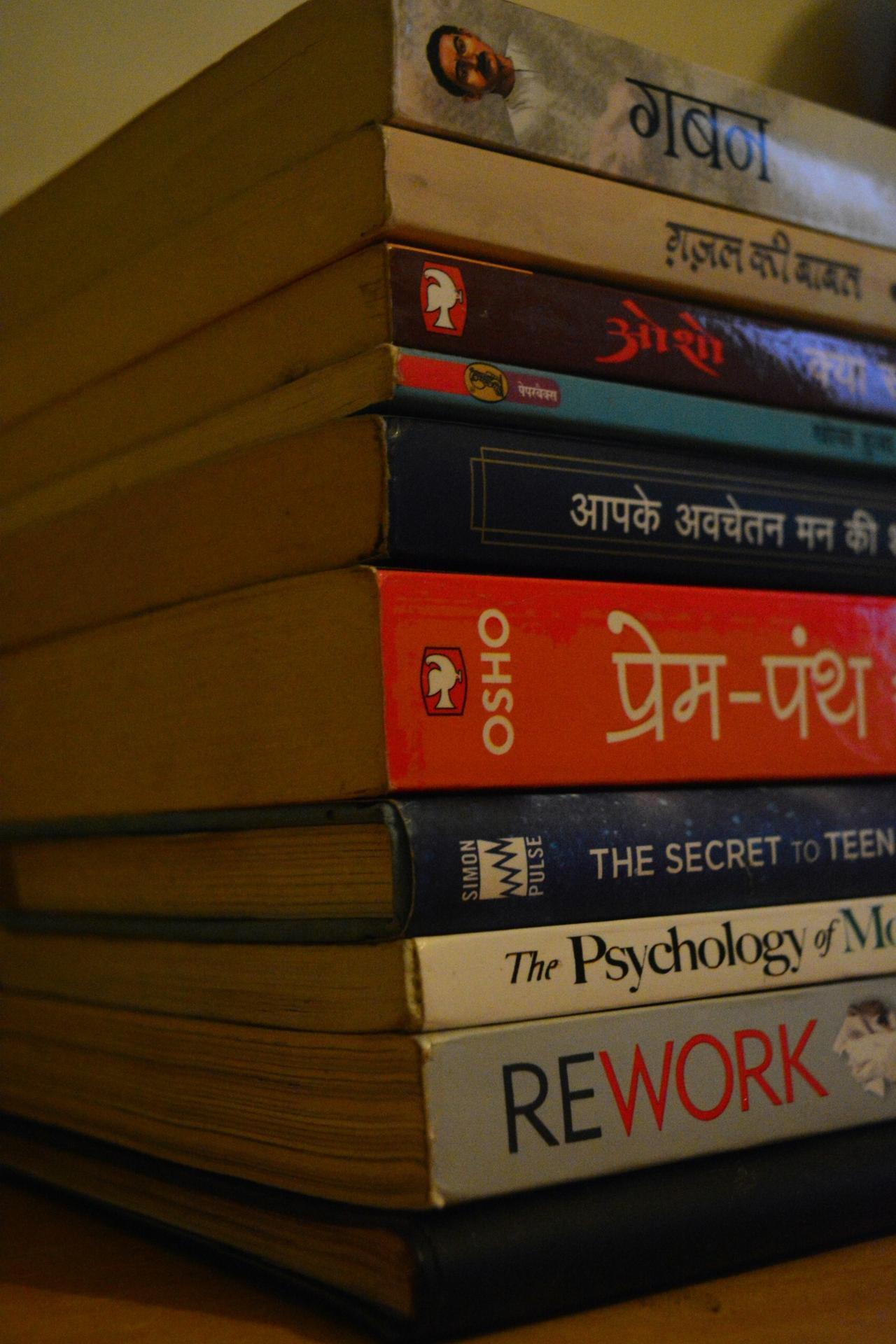 Stack of Hindi and English books on a table, representing learning Hindi sentence structure, verbs, and grammar through reading.