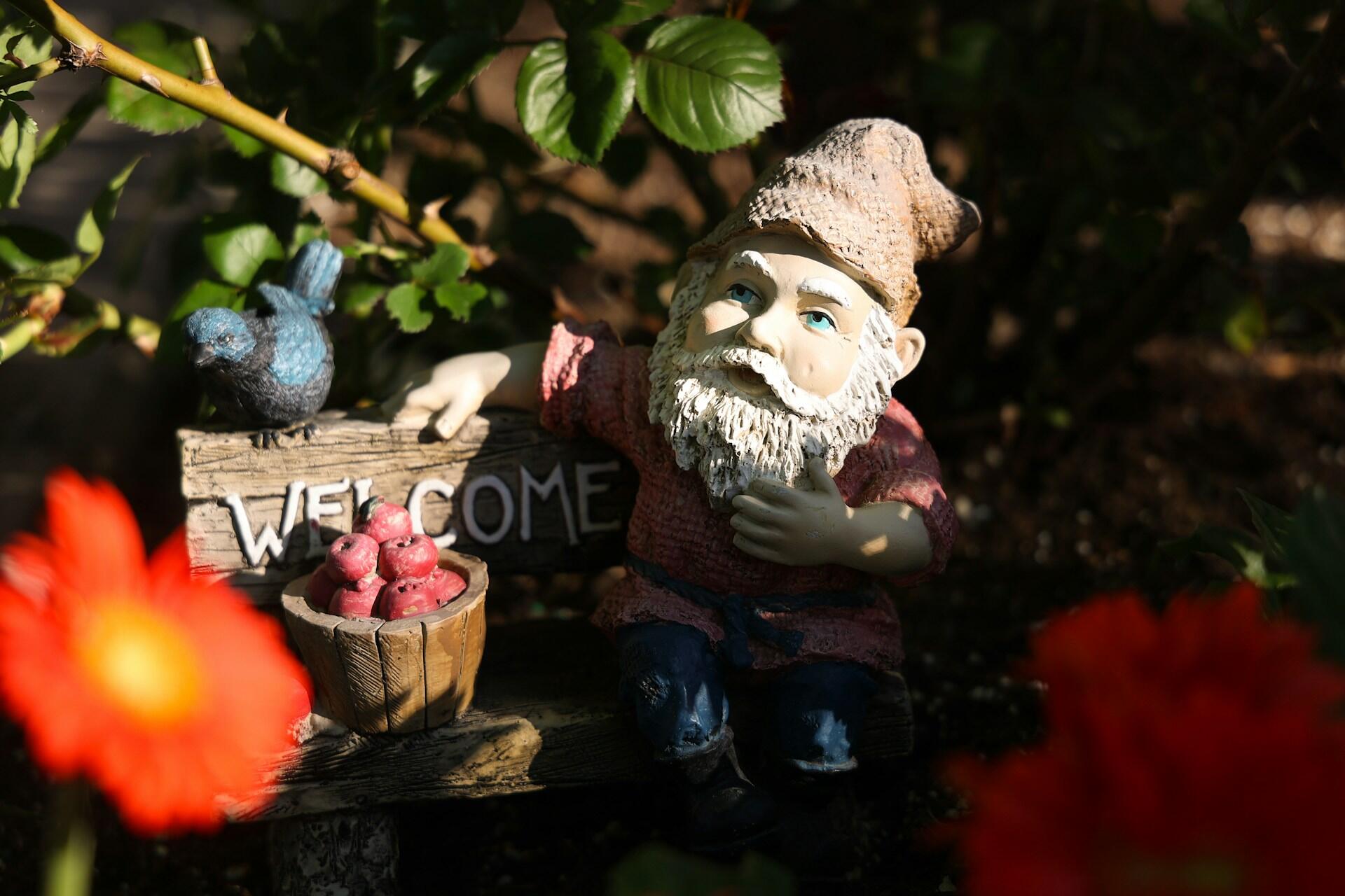A gnome on a bench next to some flowers. 
