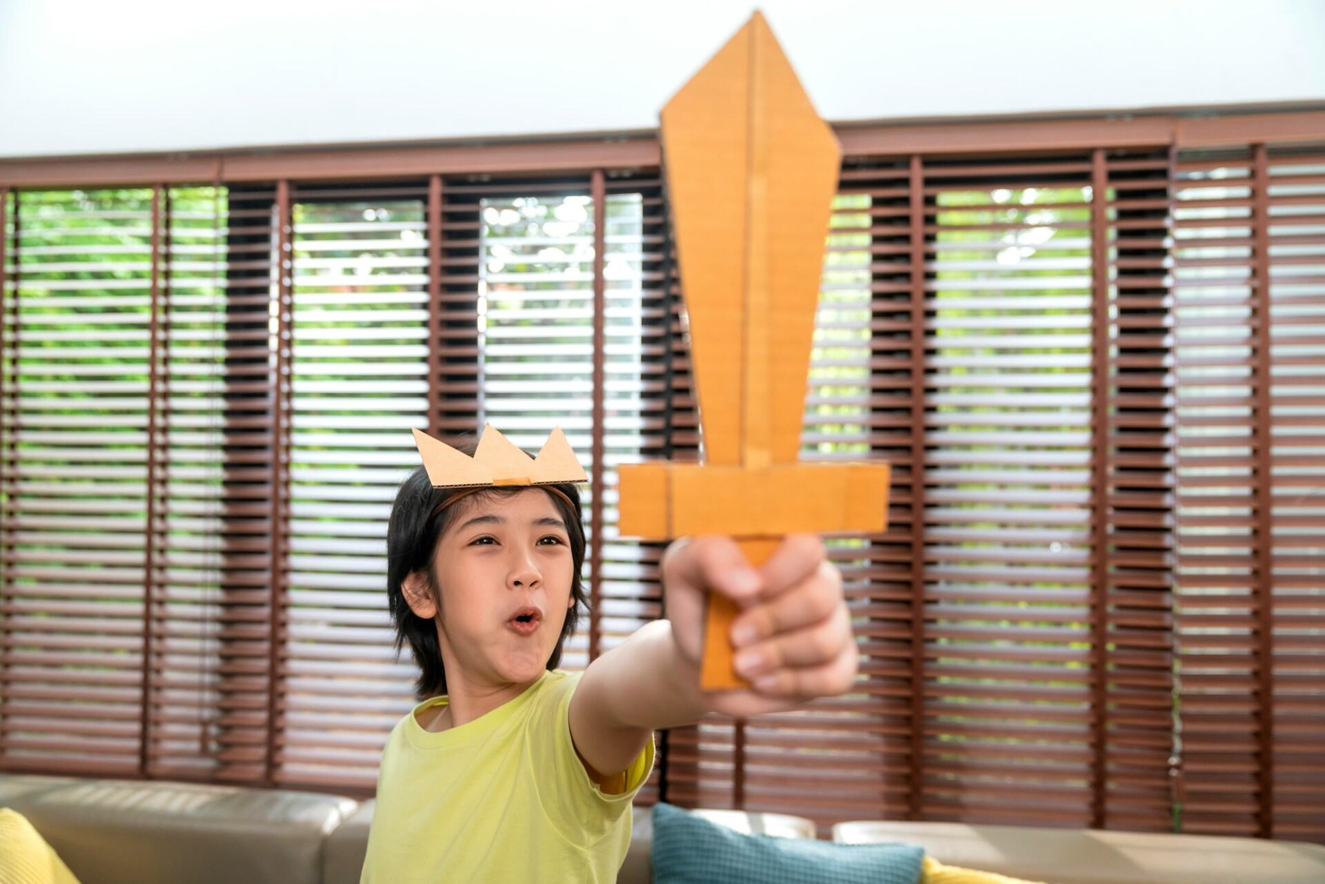A child wearing a paper crown and holding a short sword aloft.