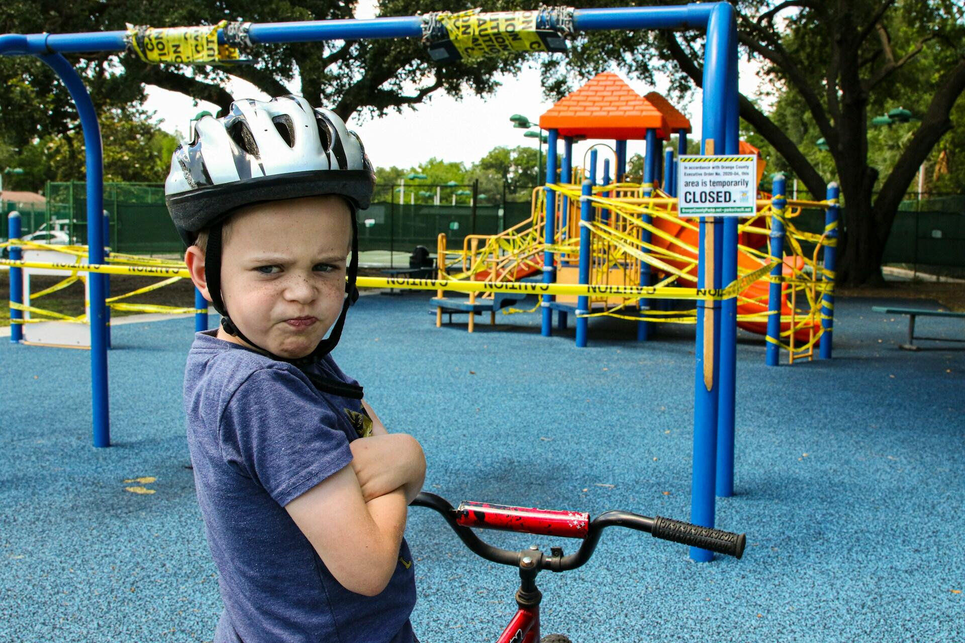 An angry child wearing a bike helmet, with his arms crossed. 