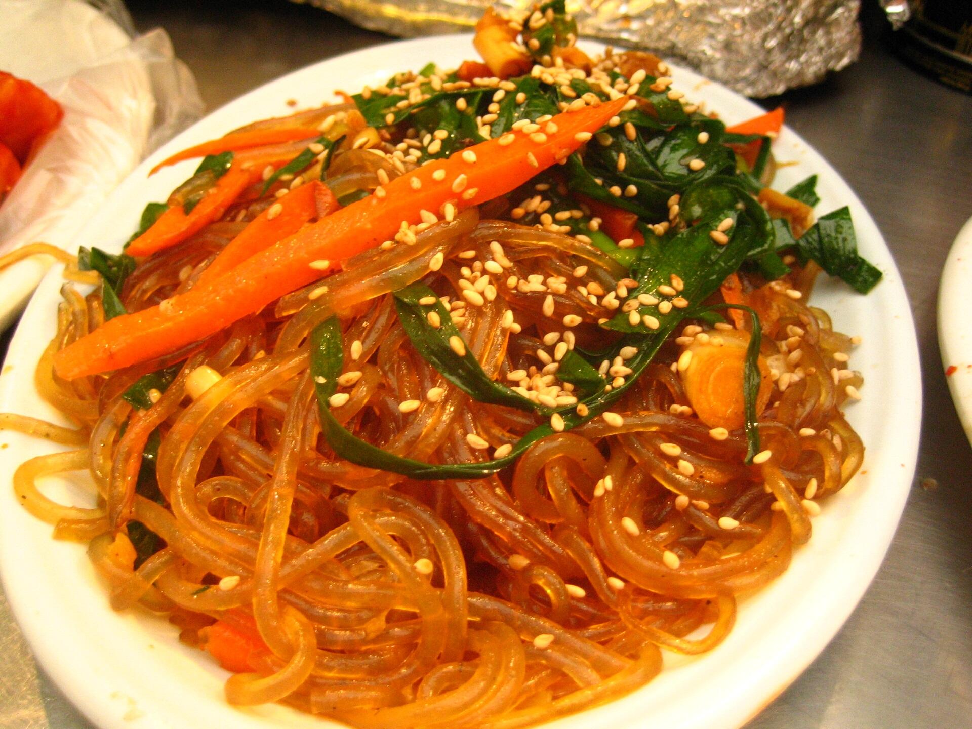A plate of noodles with thin carrot slices and greenery decorating it. 