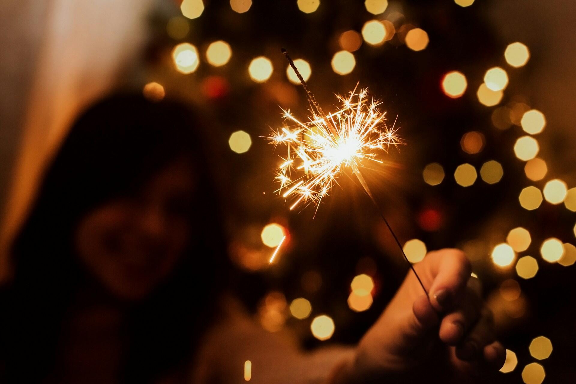 A woman holds up a sparkler against a festive background.