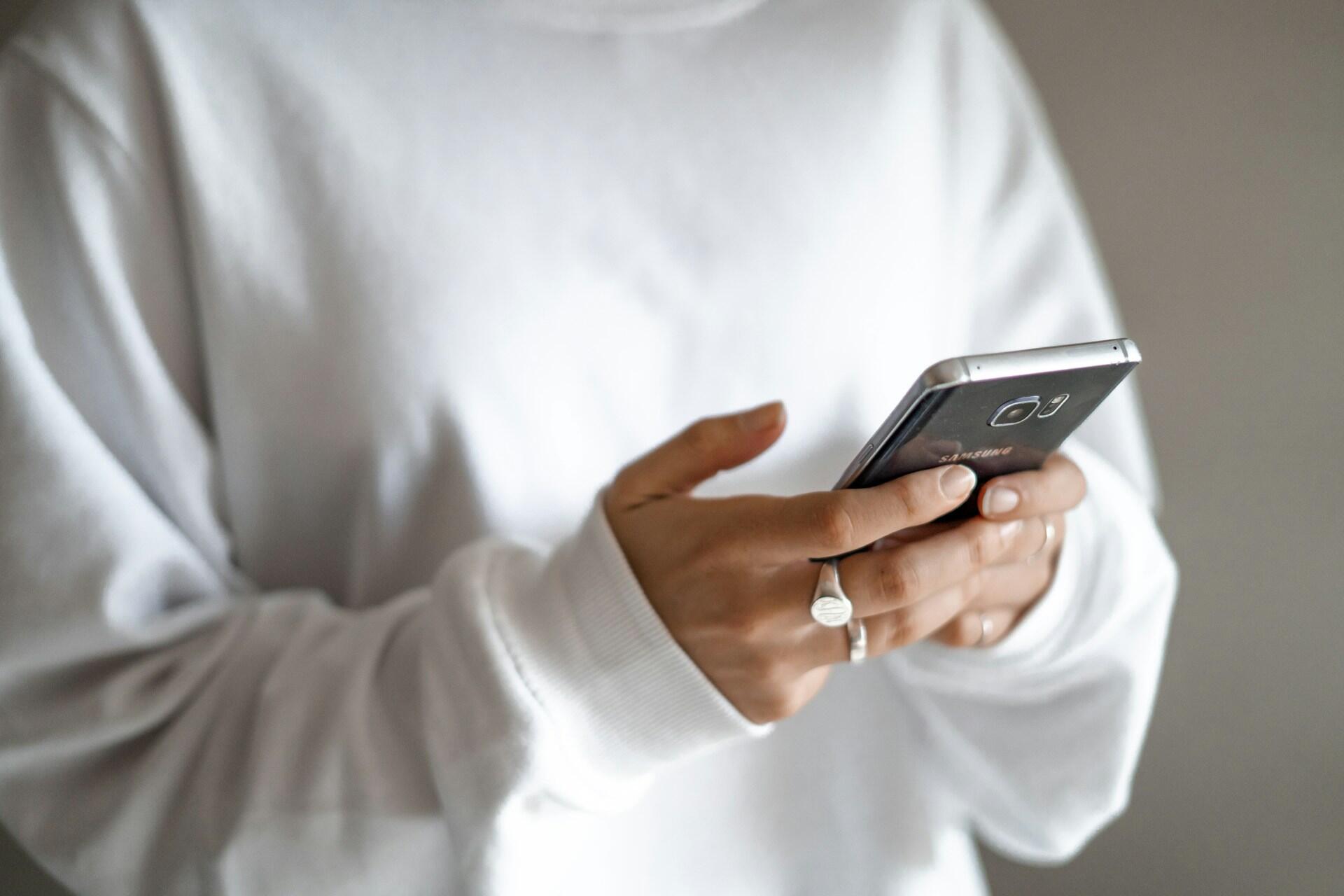 A person in a white jumper holds a smartphone. 