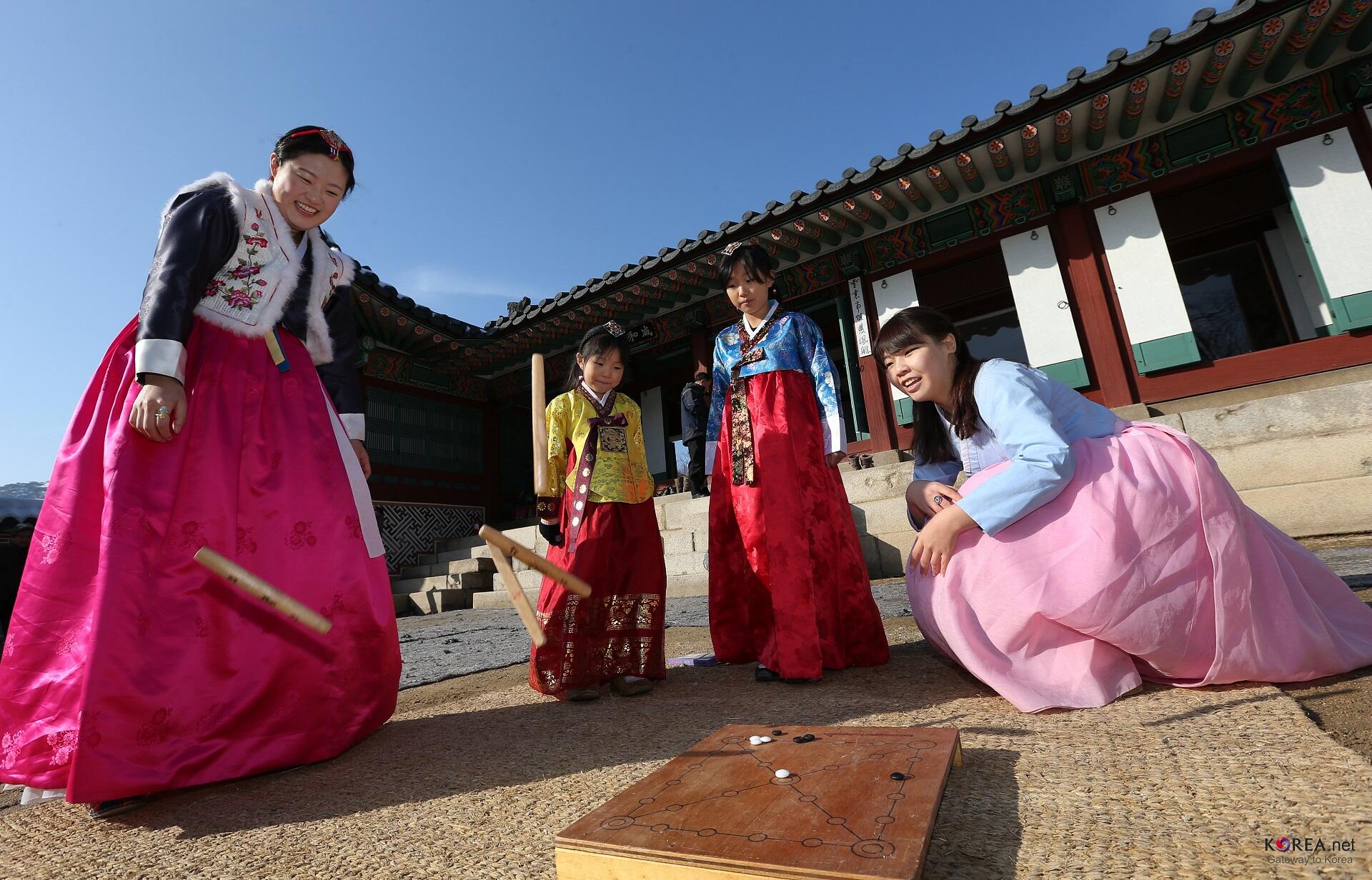 Two women wearing hanbok play a game while two girls look on.