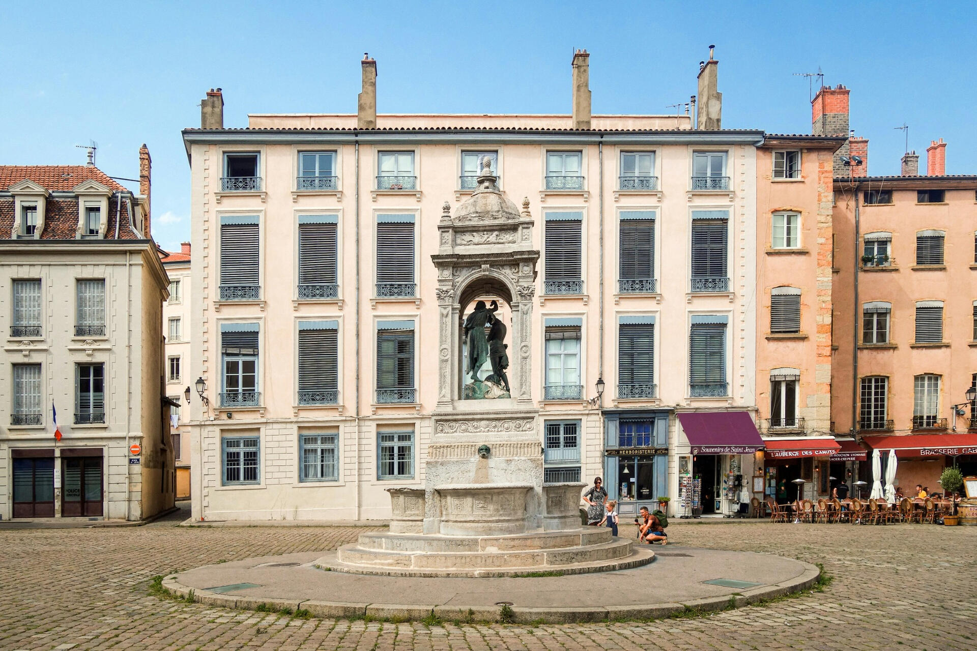 Historic French town square with traditional architecture and a central monument under a clear blue sky