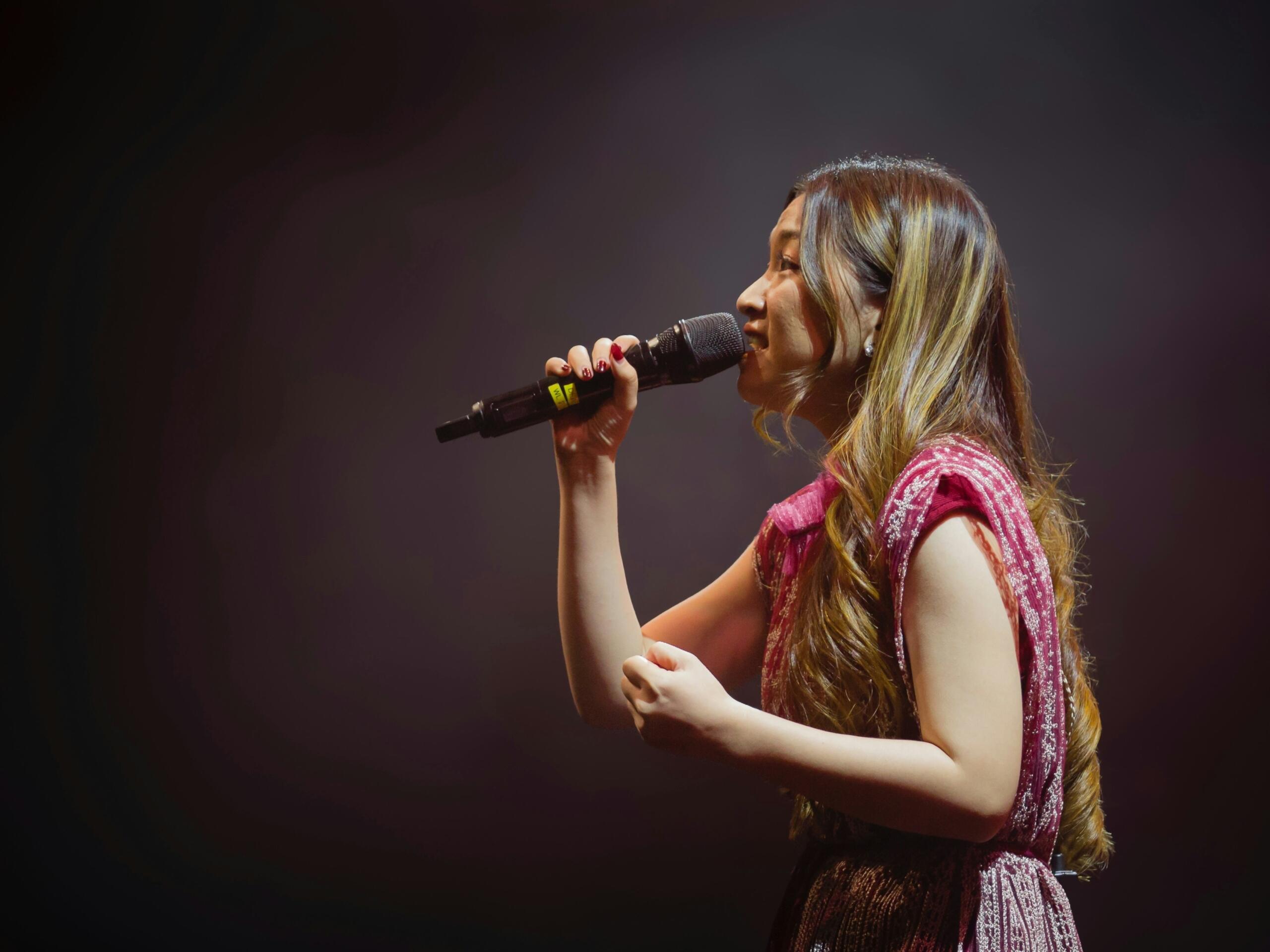 A woman passionately singing into a microphone on stage, with bright lights illuminating her face.