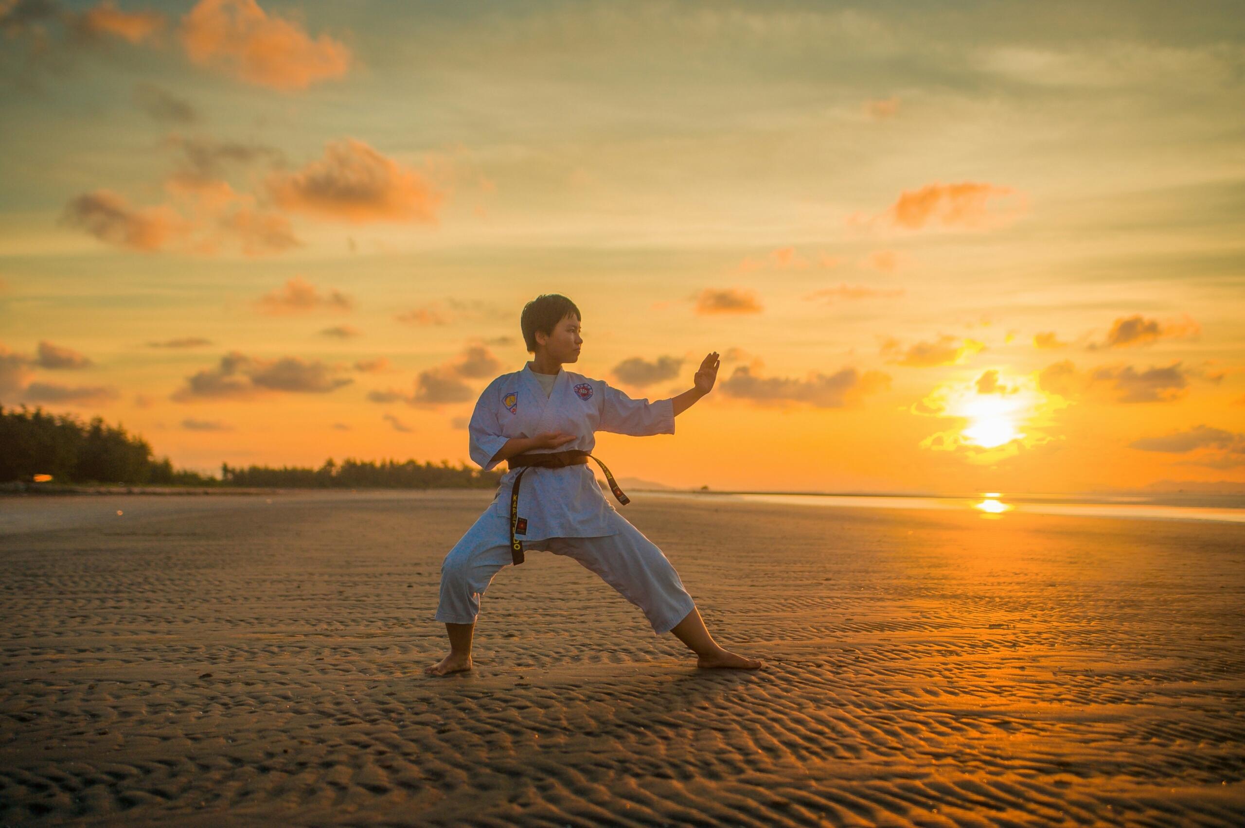 A boy doing a karate routine on a beach during the golden hour.
