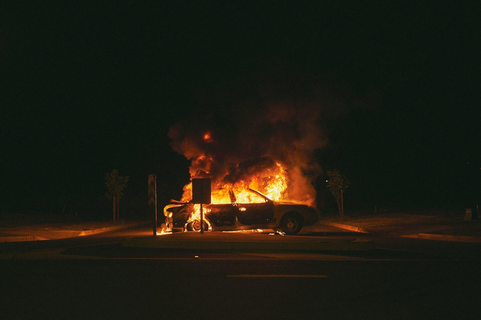 A car on fire at night by a street sign. 