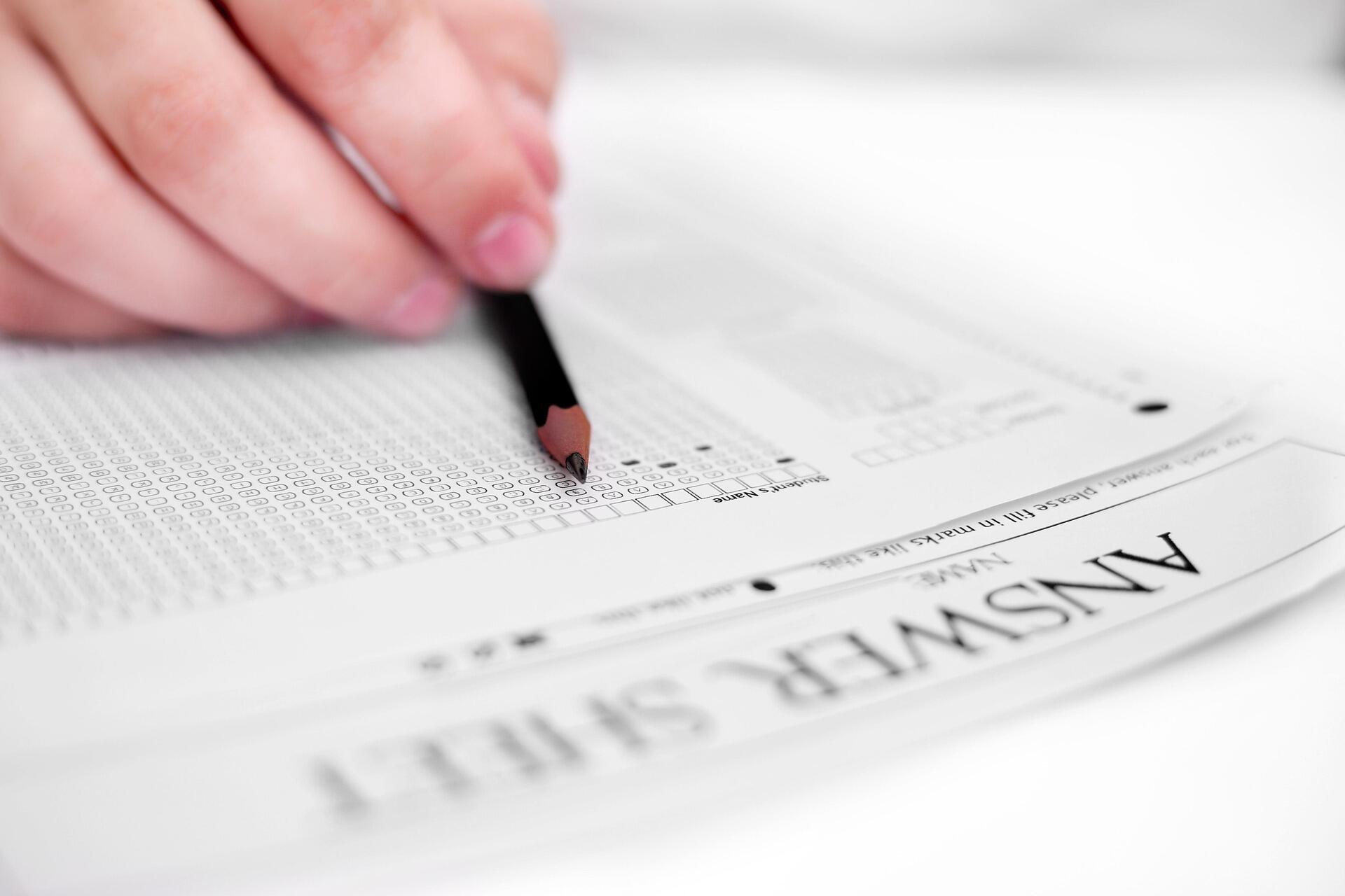 Hand holding pencil filling out a multiple-choice answer sheet for a test or exam.