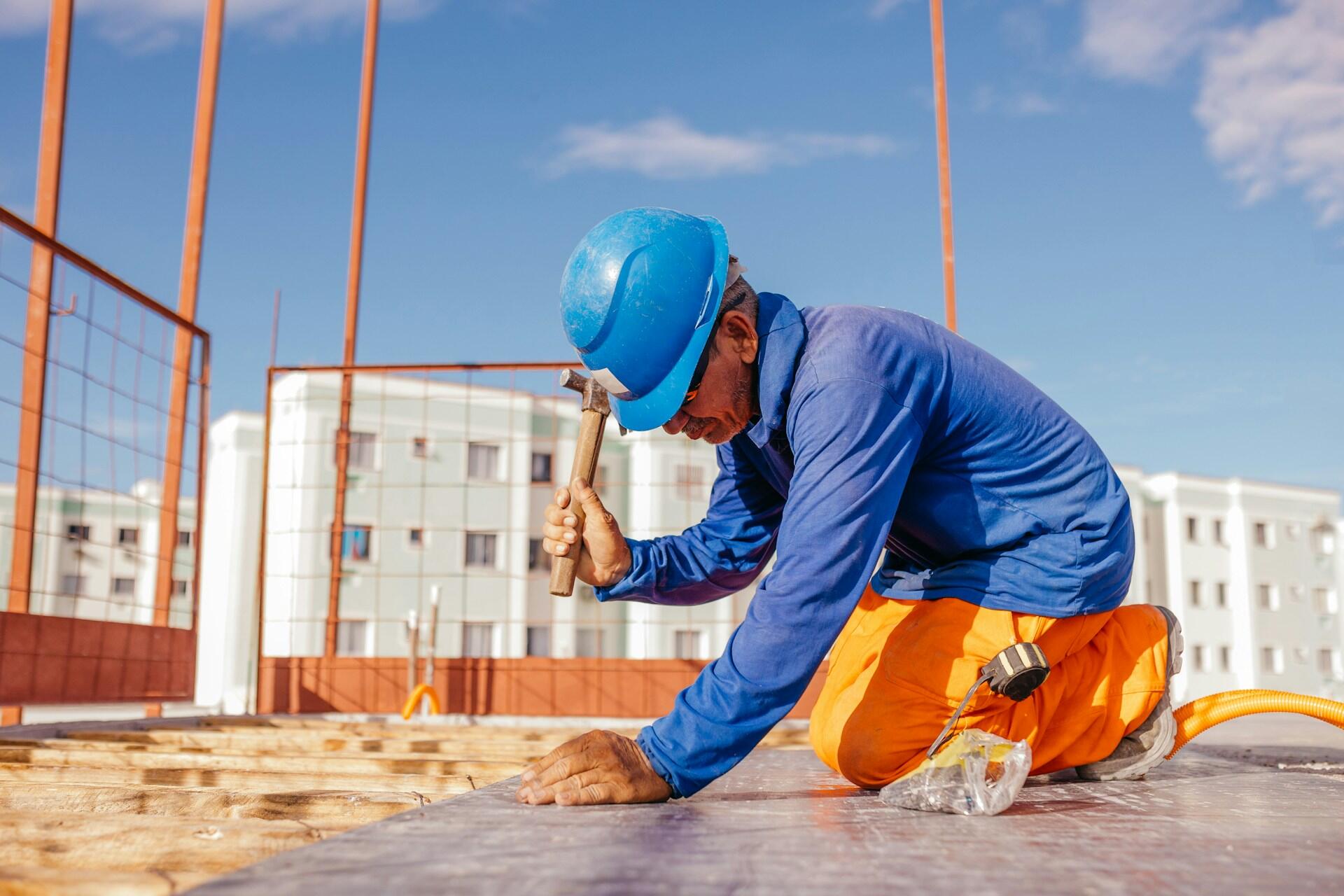 A person wearing a hard hat kneels while swinging a hammer. 