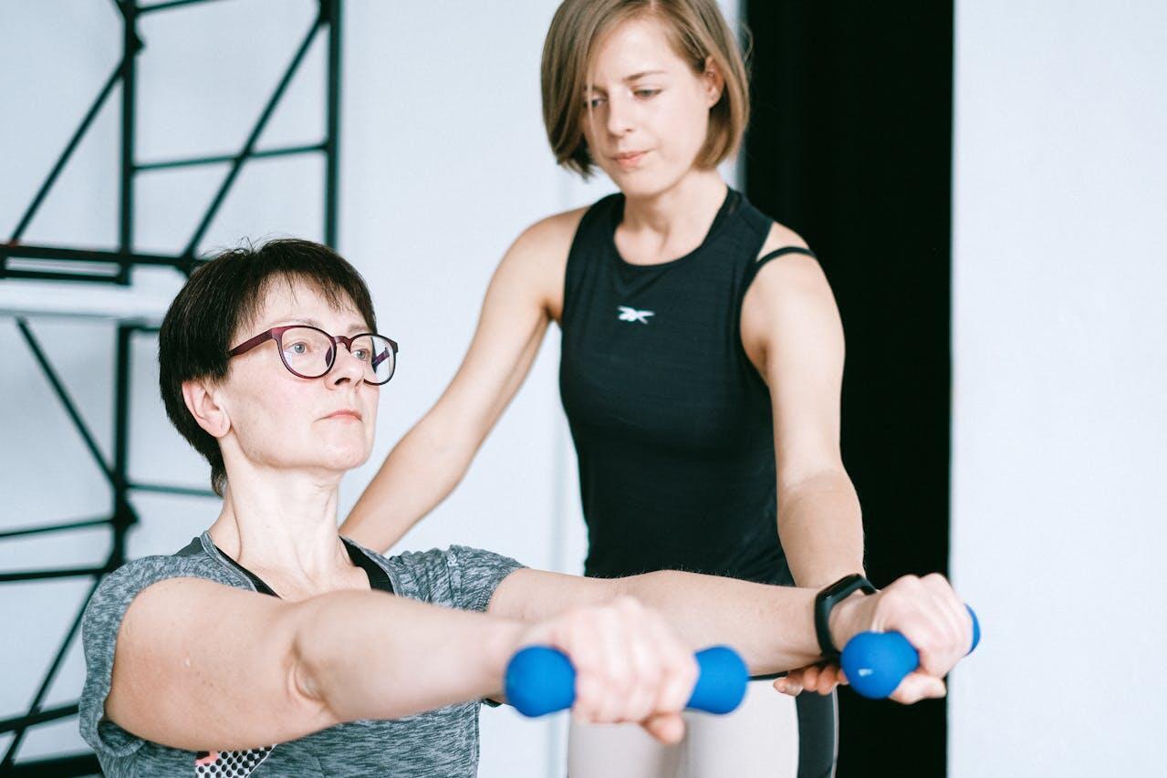 woman lifting weights with the help of personal trainer