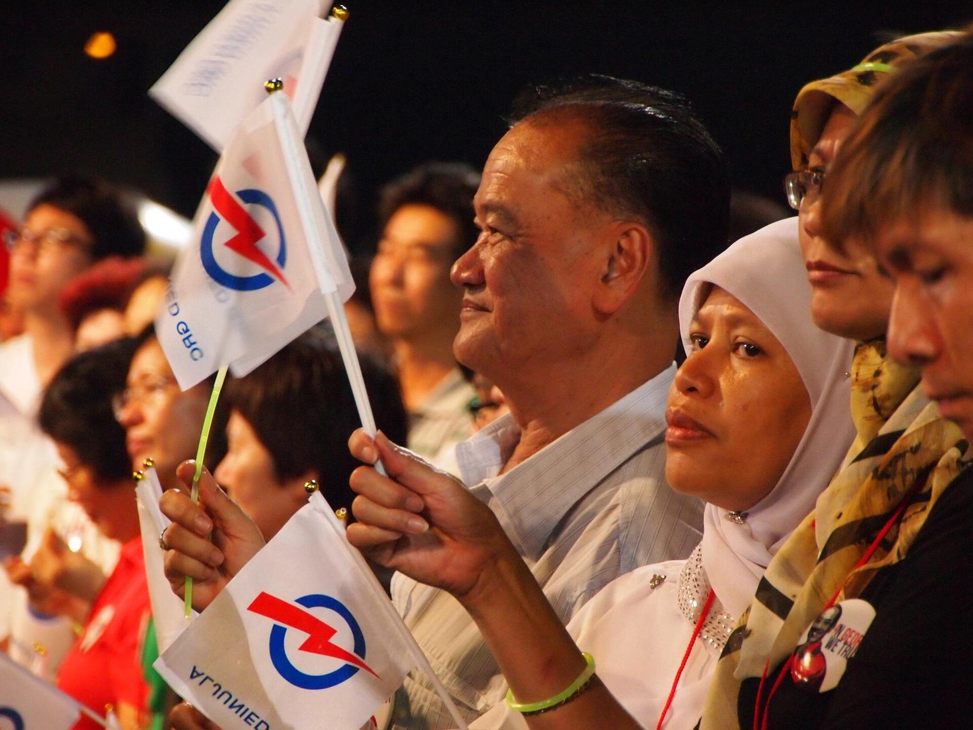 People holding white flags with a blue circle and red lightning bolt symbol at a nighttime event or rally.