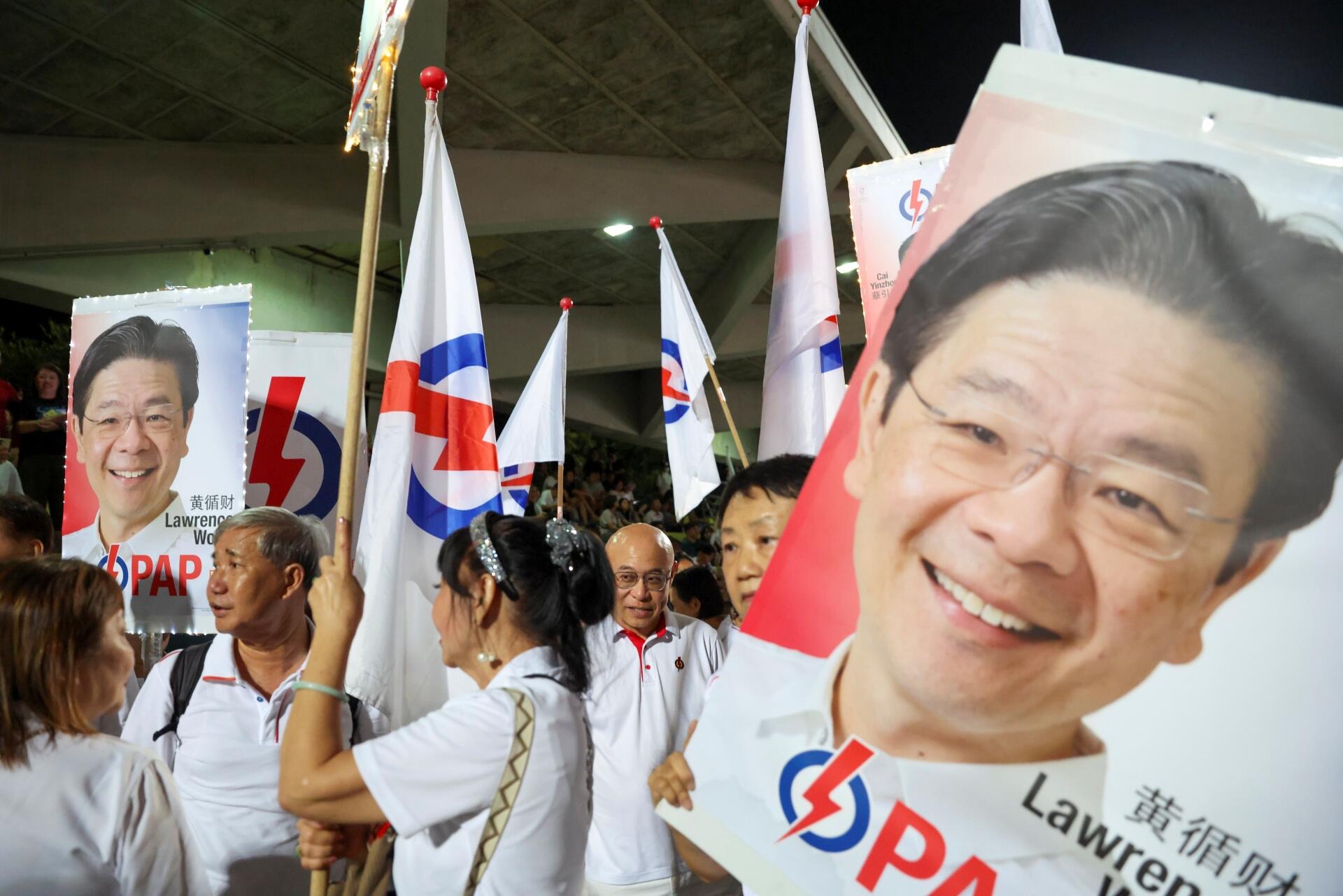 A group of people holding political party flags and posters at a nighttime outdoor rally or event.