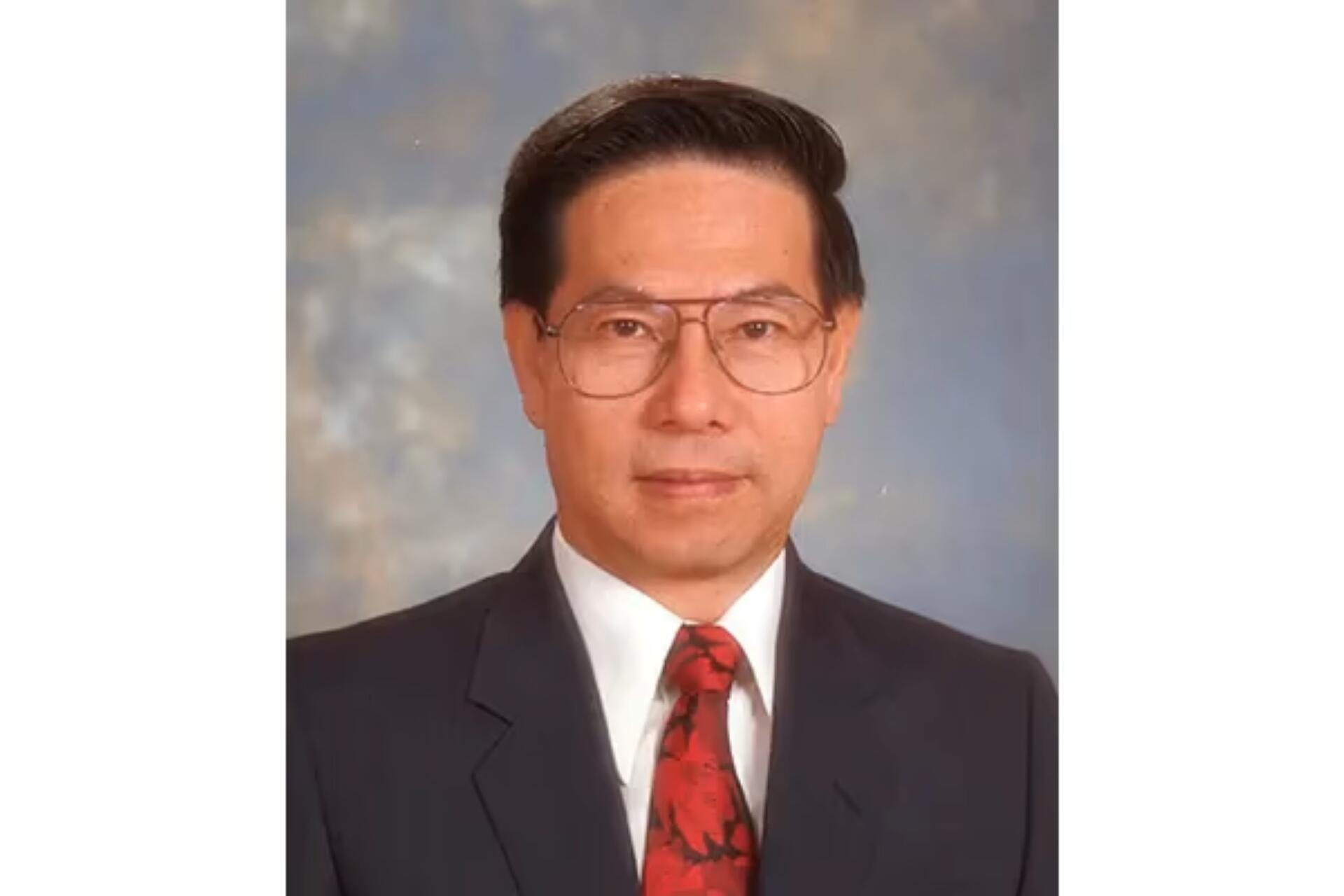 Portrait of Ong Teng Cheong in a dark suit jacket, white shirt, and red patterned tie against a blue-gray mottled backdrop.
