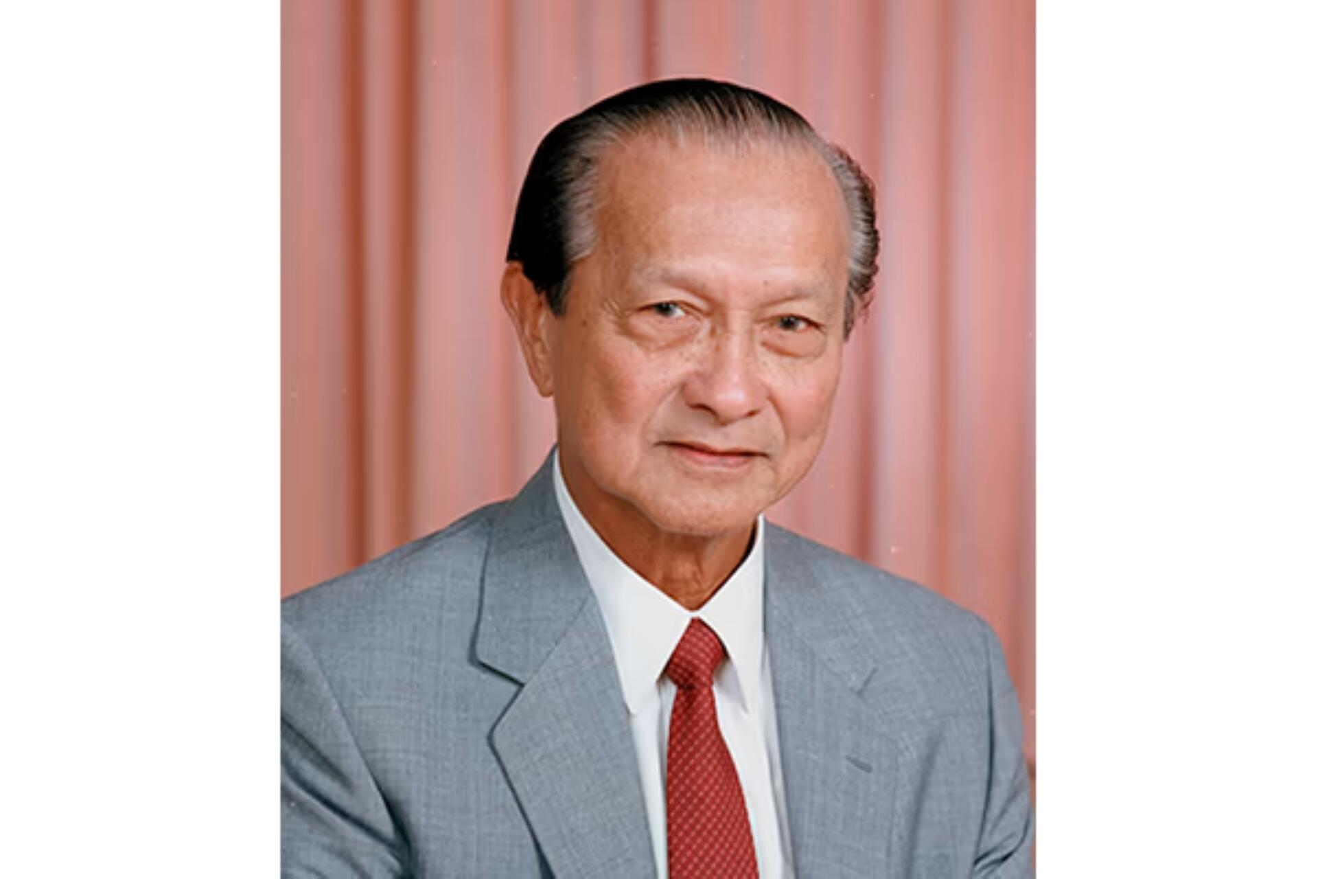 Wee Kim Wee in a light gray suit, white shirt, and red tie standing in front of a peach-colored curtain background.