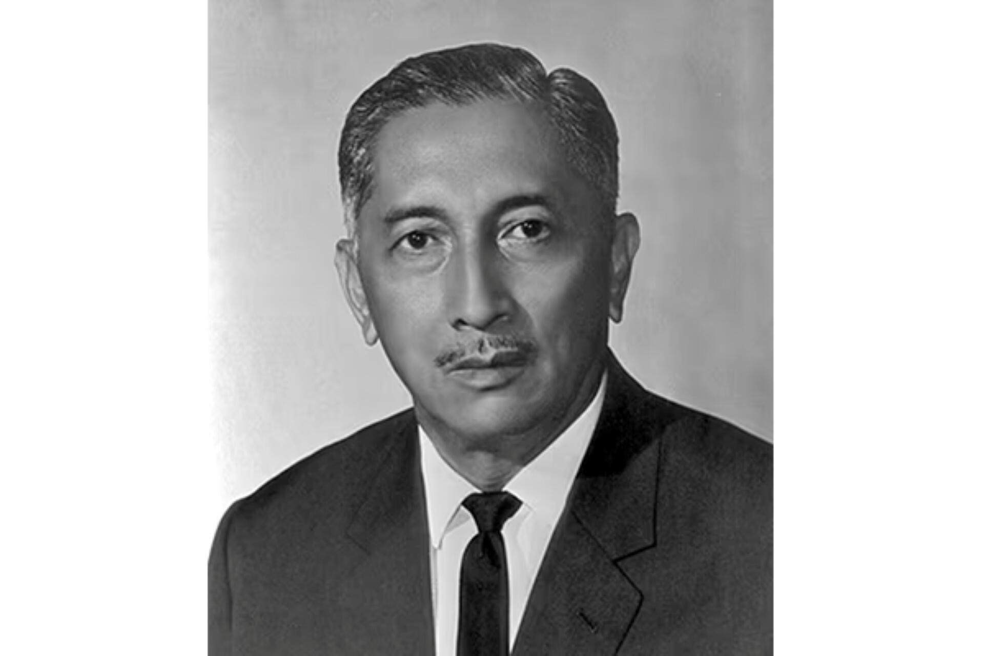 Black and white portrait of Yusof Ishak wearing a dark suit, white shirt, and black tie against a plain background.
