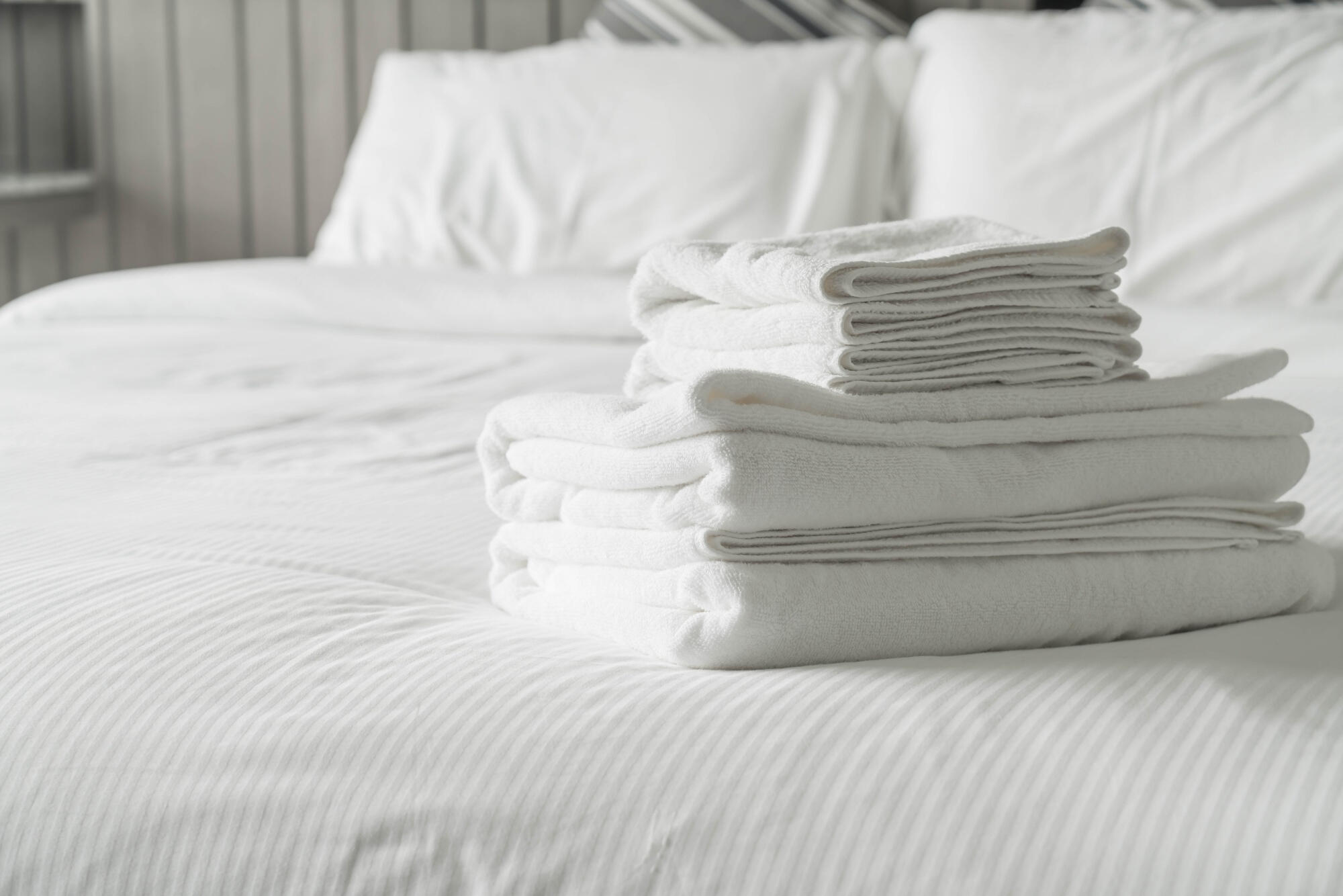 A neatly arranged stack of folded towels placed on a neatly made bed.